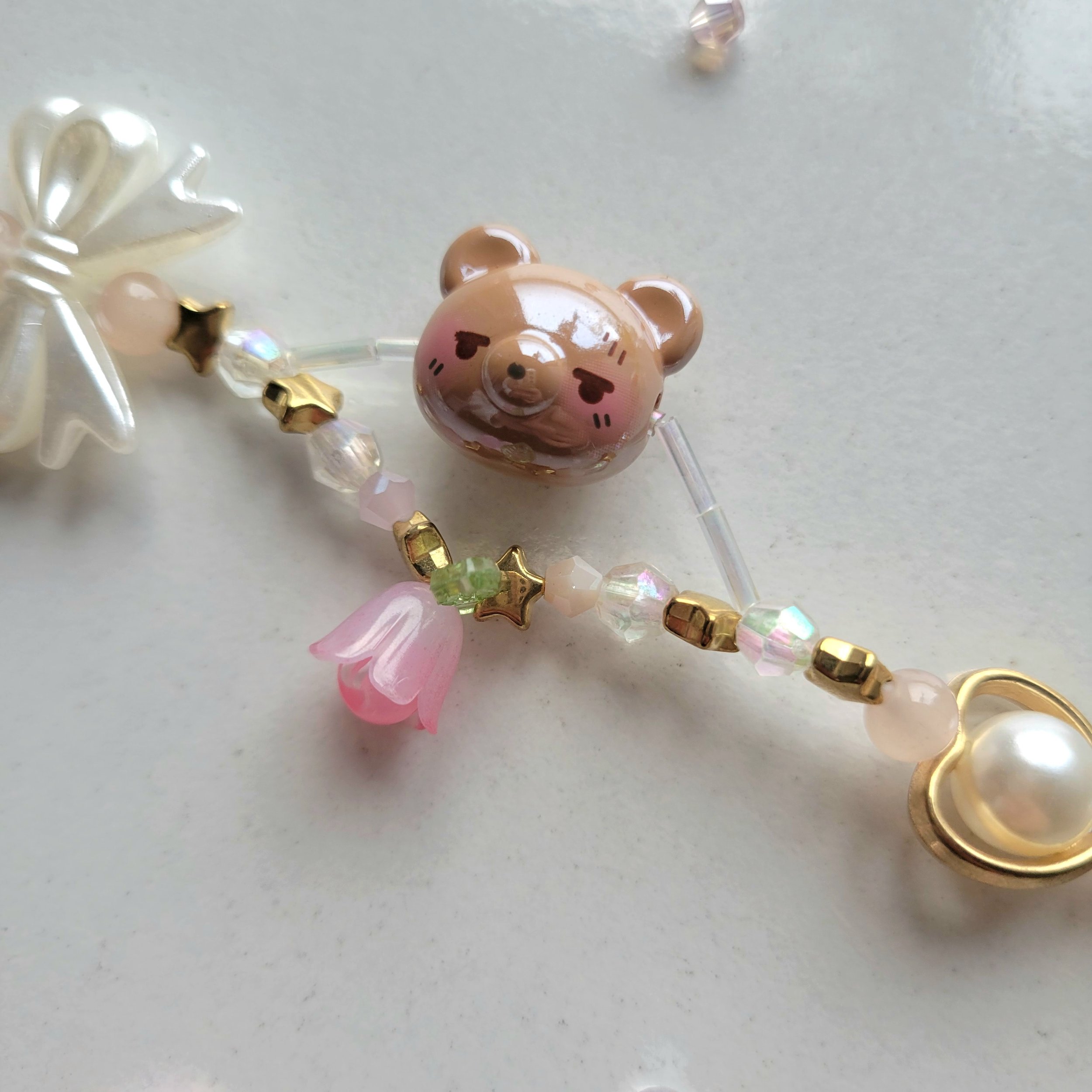 Image of a brown bear bead on a dual string bracelet. The bottom string layer has a pink flower attached and golden stars.