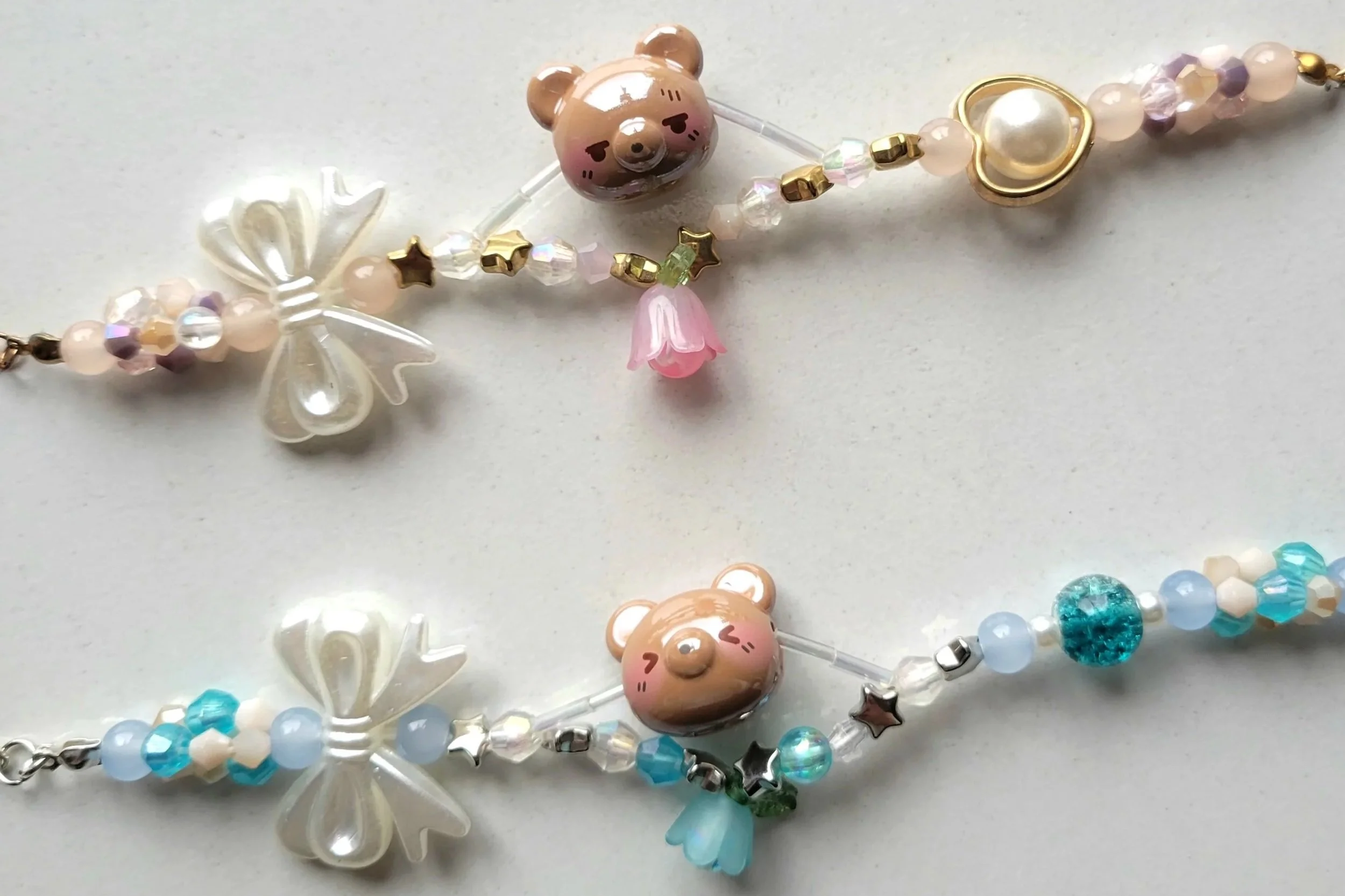 Close-up of a colorful beaded bracelet with star-shaped, pearl, and bear-shaped charms, including a pink bear with a floral dress and heart-shaped face, on a light background.