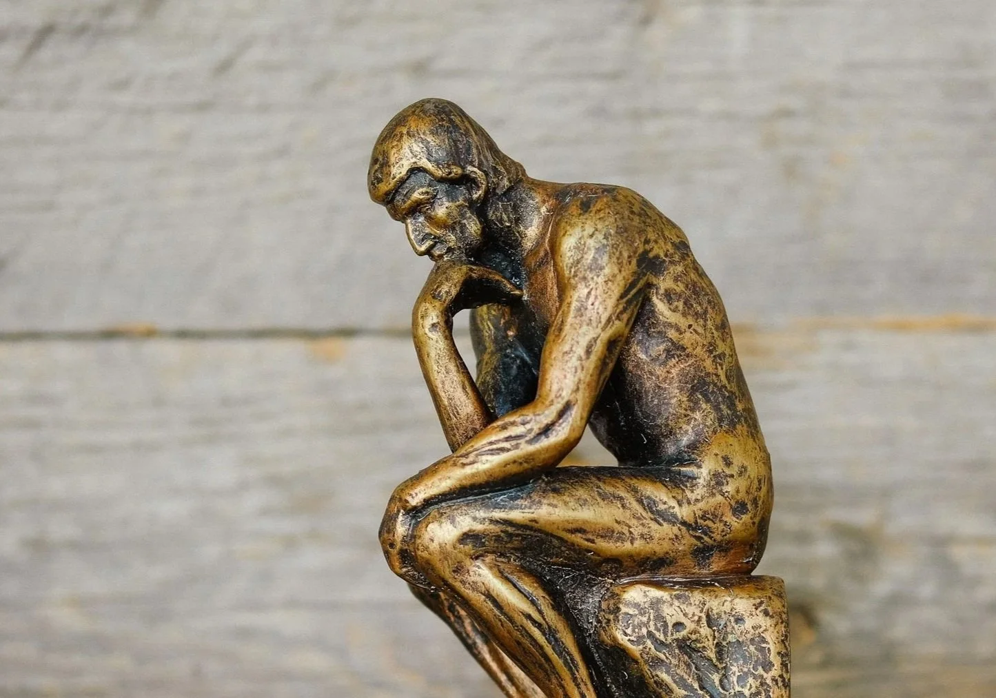 Bronze sculpture of a man sitting with his chin resting on his hand in a contemplative pose.