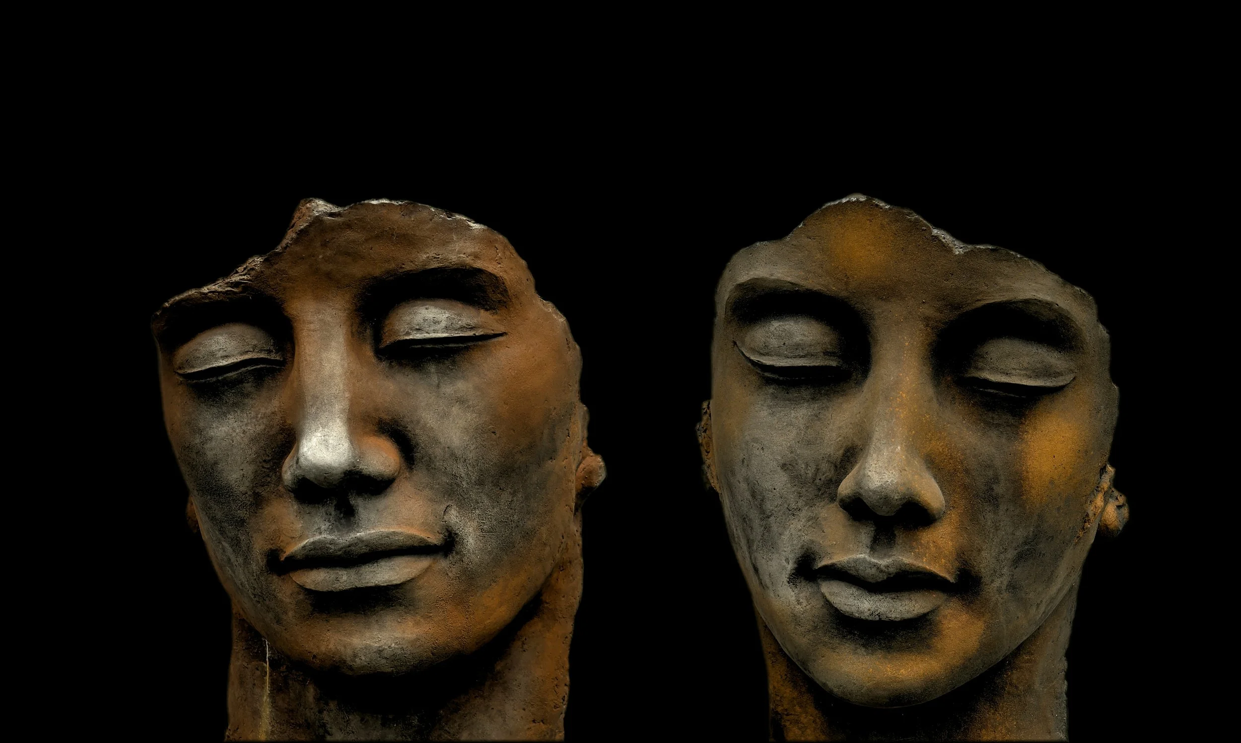 Two ancient stone or ceramic heads with closed eyes and serene expressions, positioned closely against a black background.