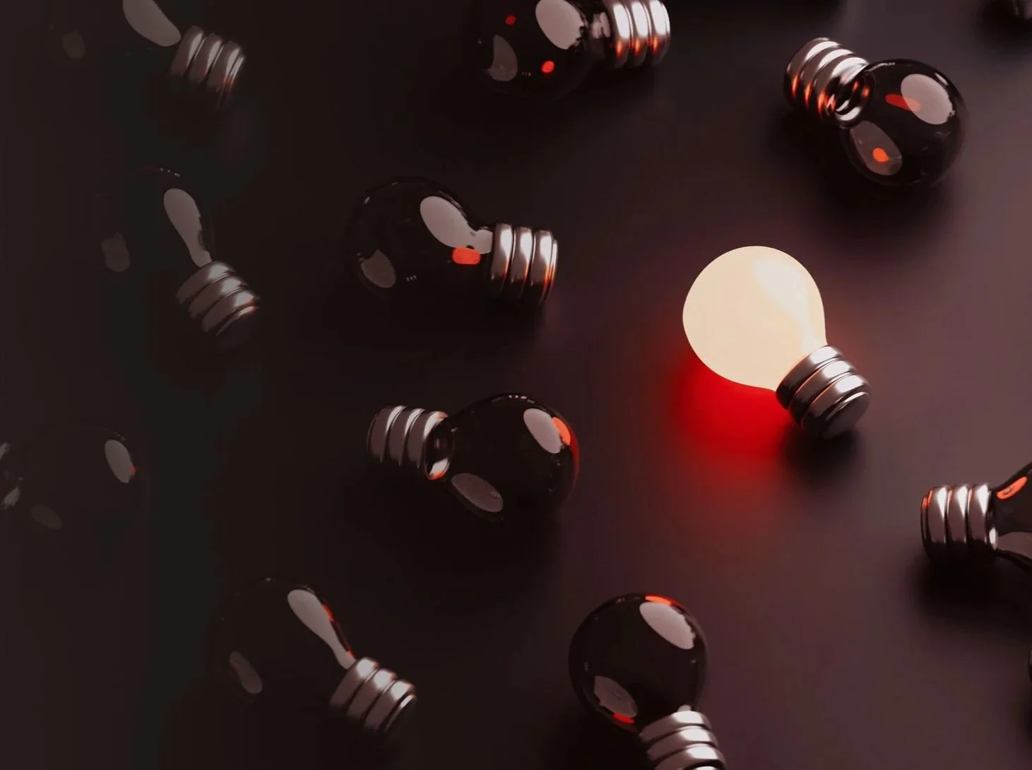 Multiple black light bulbs with metallic screw bases scattered on a dark surface, with one illuminated bulb emitting red light.