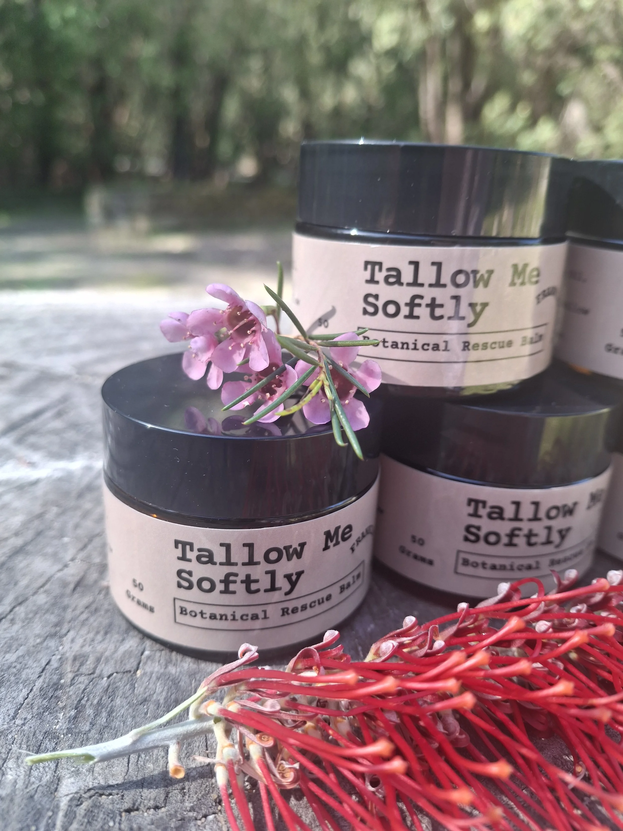 A close-up product image of Frankincense Rescue Botanical Balm resting on a rustic log, surrounded by the natural colours and native grevillea