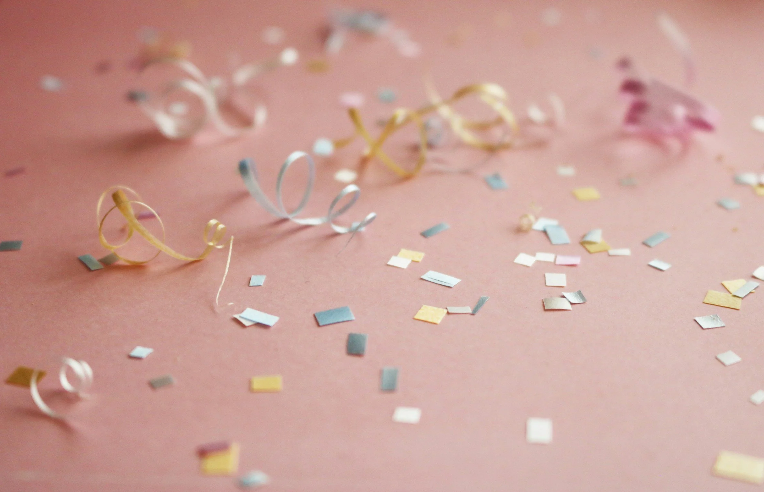 Colorful confetti and curling ribbons scattered on a pink surface.