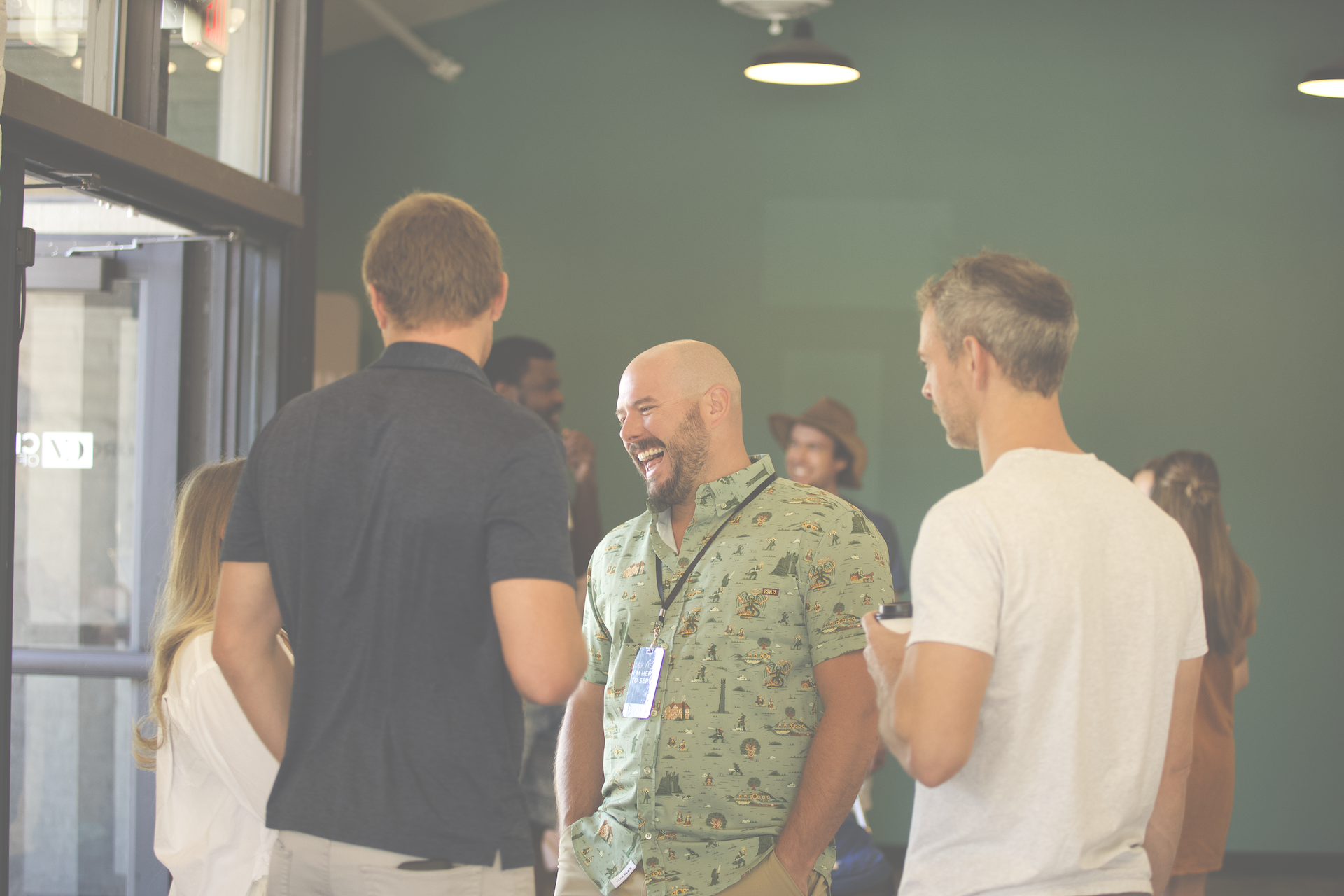 Group of people talking and smiling at an indoor event, casual attire, some wearing name badges.