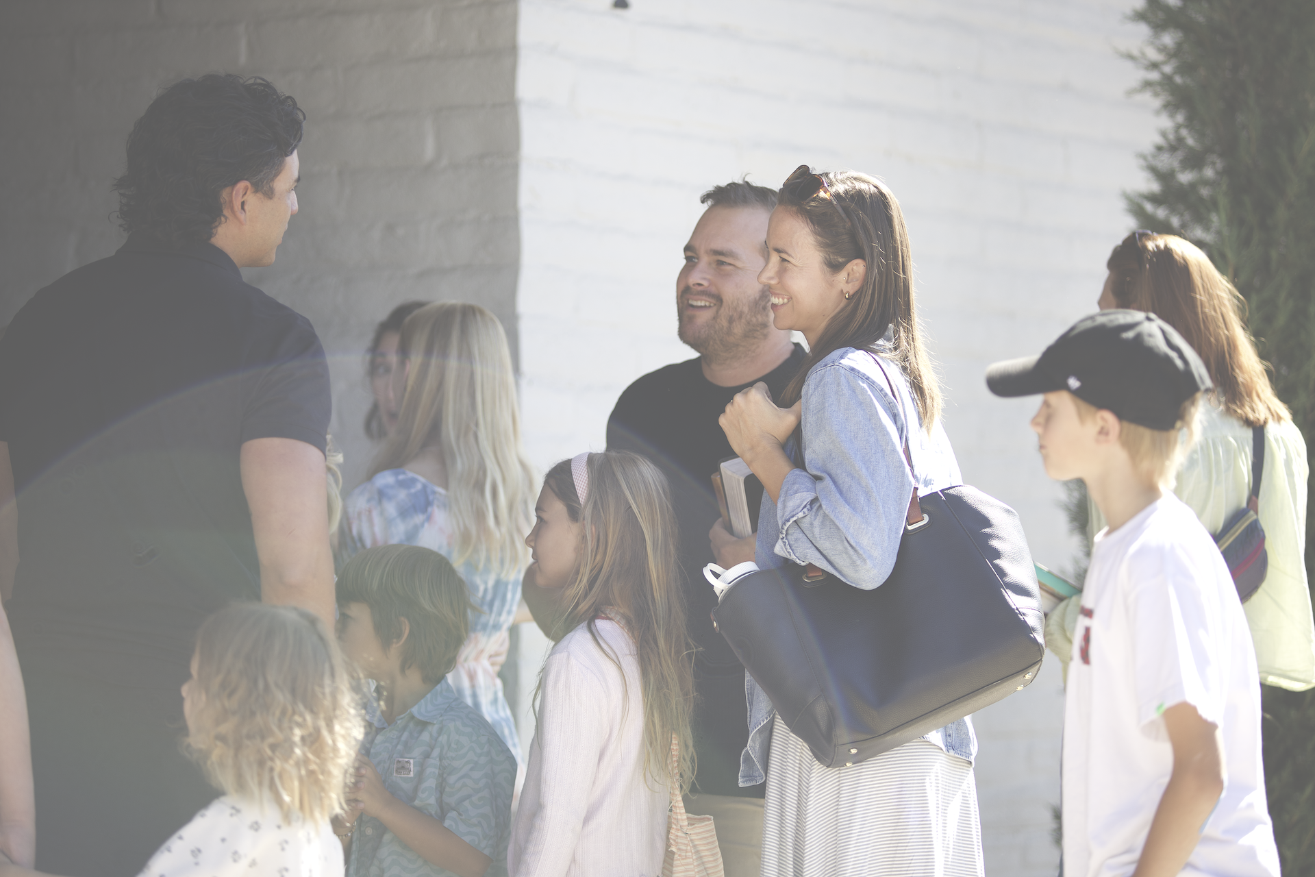 Group of children and adults smiling and talking outdoors in front of a building.