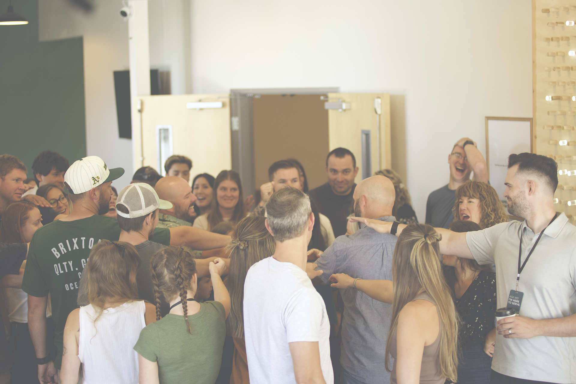 A large group of people gathered indoors, smiling, laughing, and engaging with each other in a lively and cheerful environment.