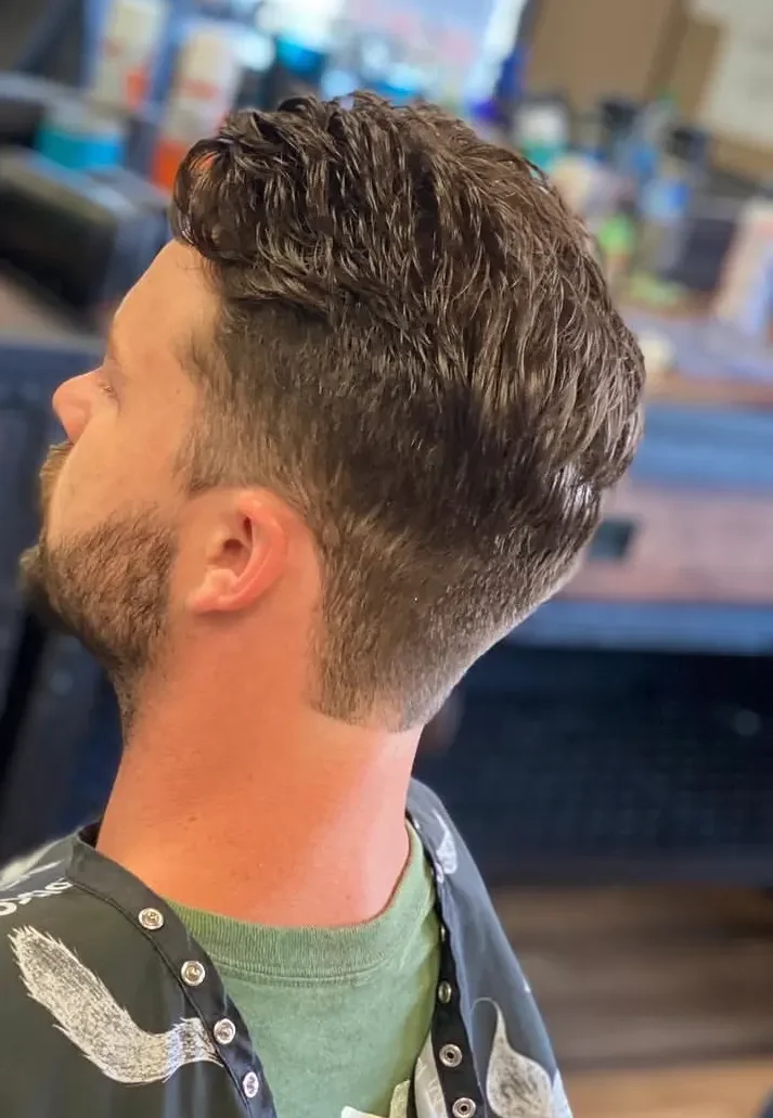 Side view of a man with a modern undercut hairstyle, short on the sides and longer on top, in a barbershop.