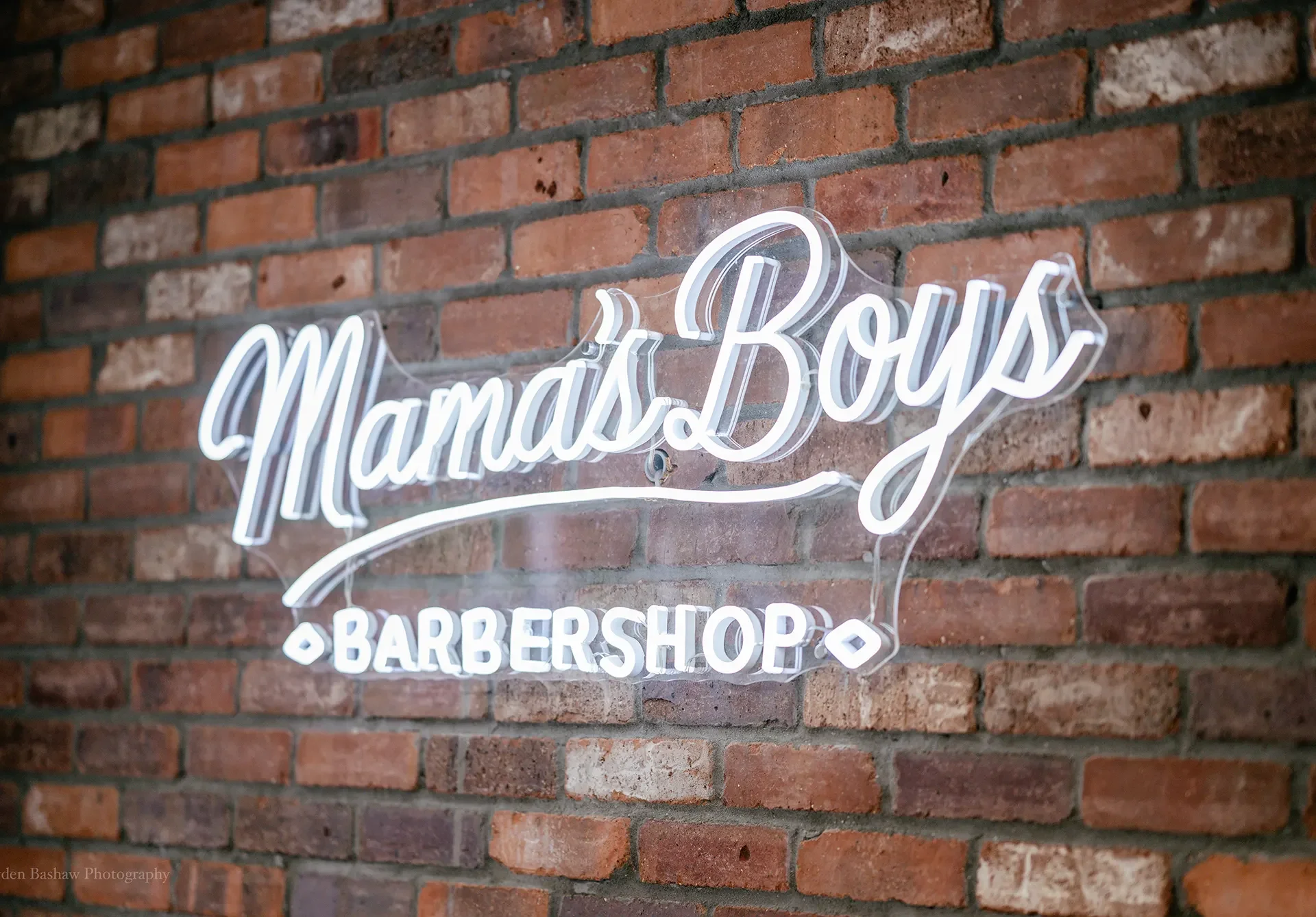 Modern interior of Mama's Boys Barbershop with barbers serving clients.