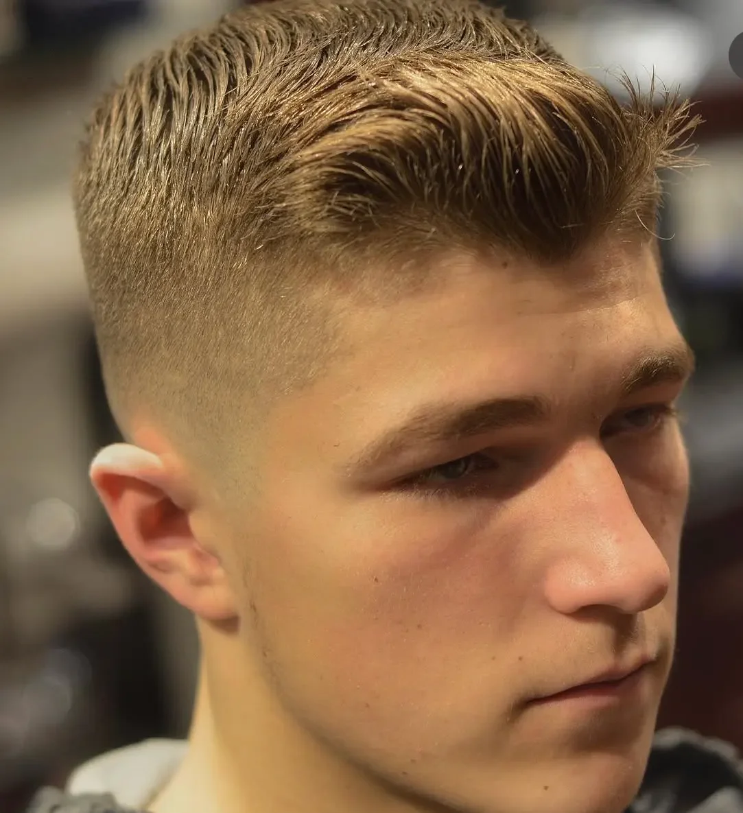 Close-up of a young man's face with a fresh, styled haircut featuring short faded sides and longer, combed hair on top.