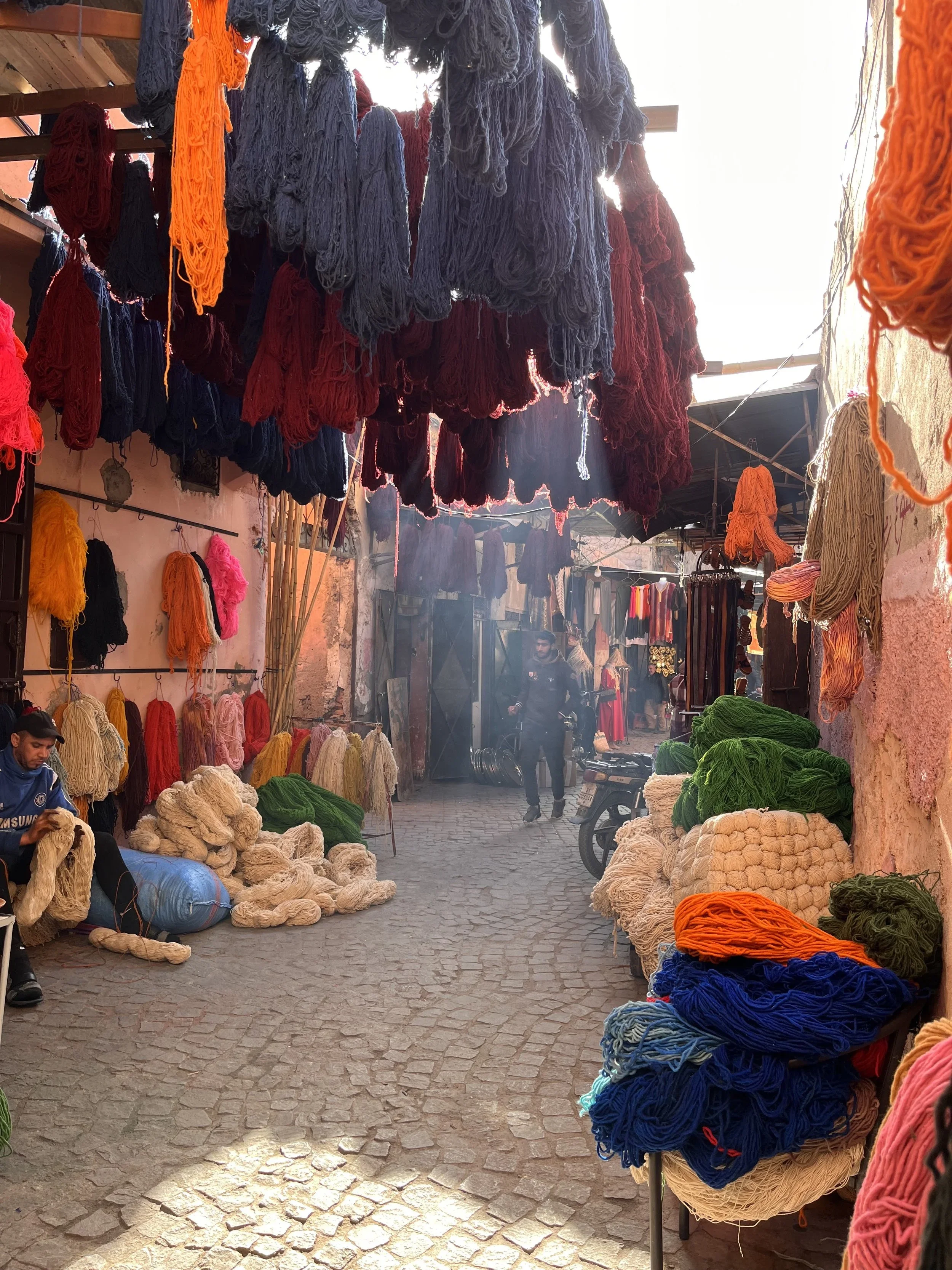 Moroccan Souk in Marrakesh filled with colourful dyed yarns and locals walking through the narrow streets.