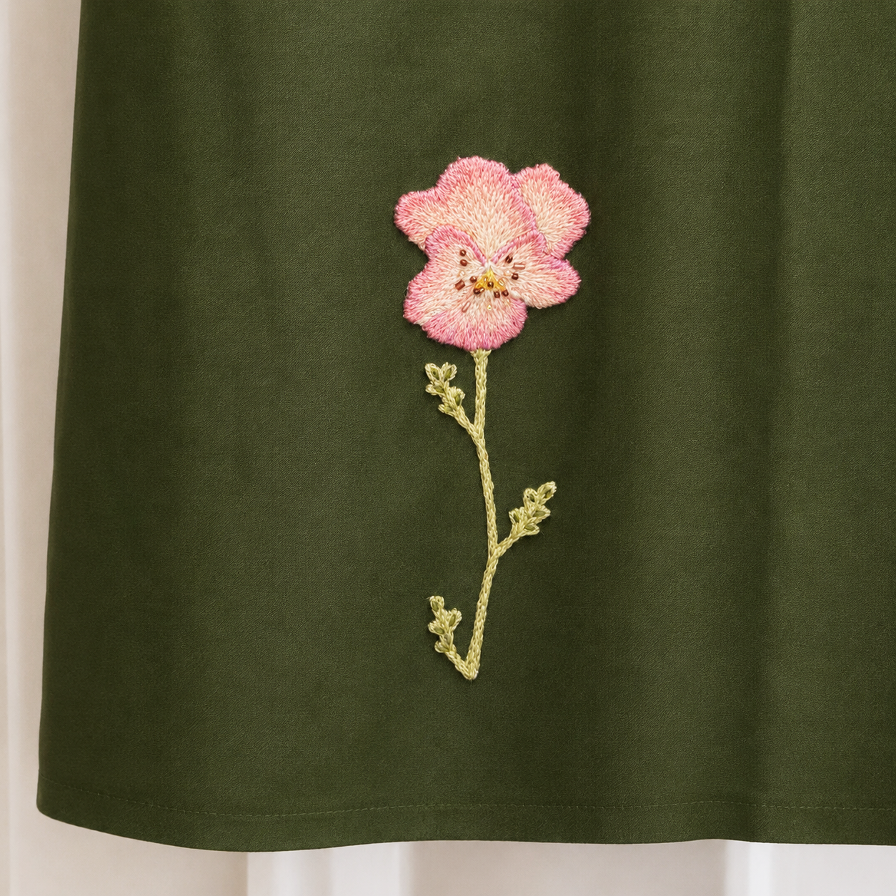 Embroidery of a pink and cream flower on a dark green fabric.