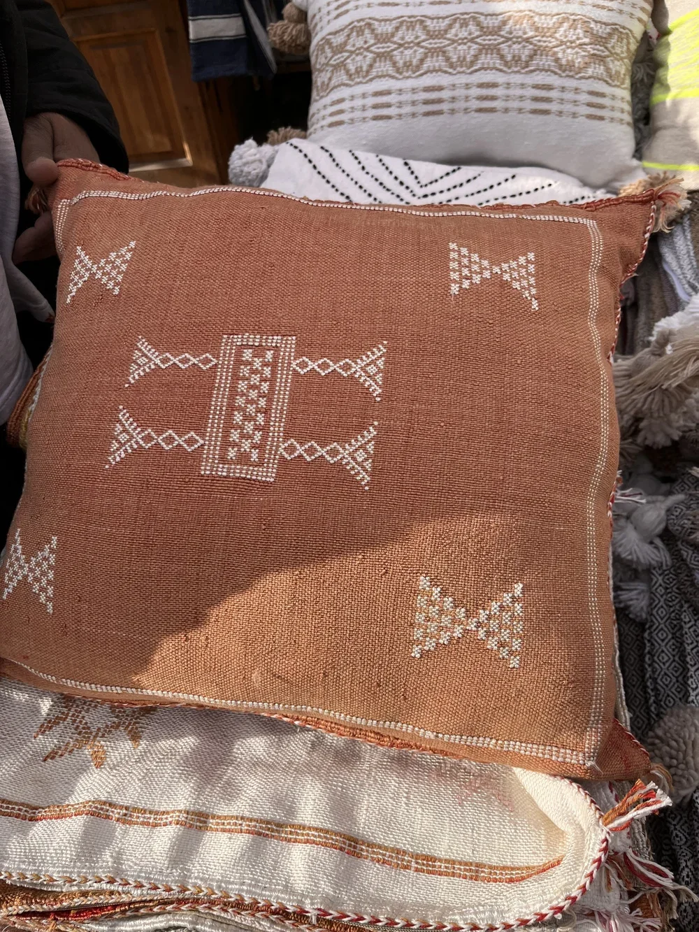 Peach coloured hand-woven cushion with white geometric design in a Moroccan souk.