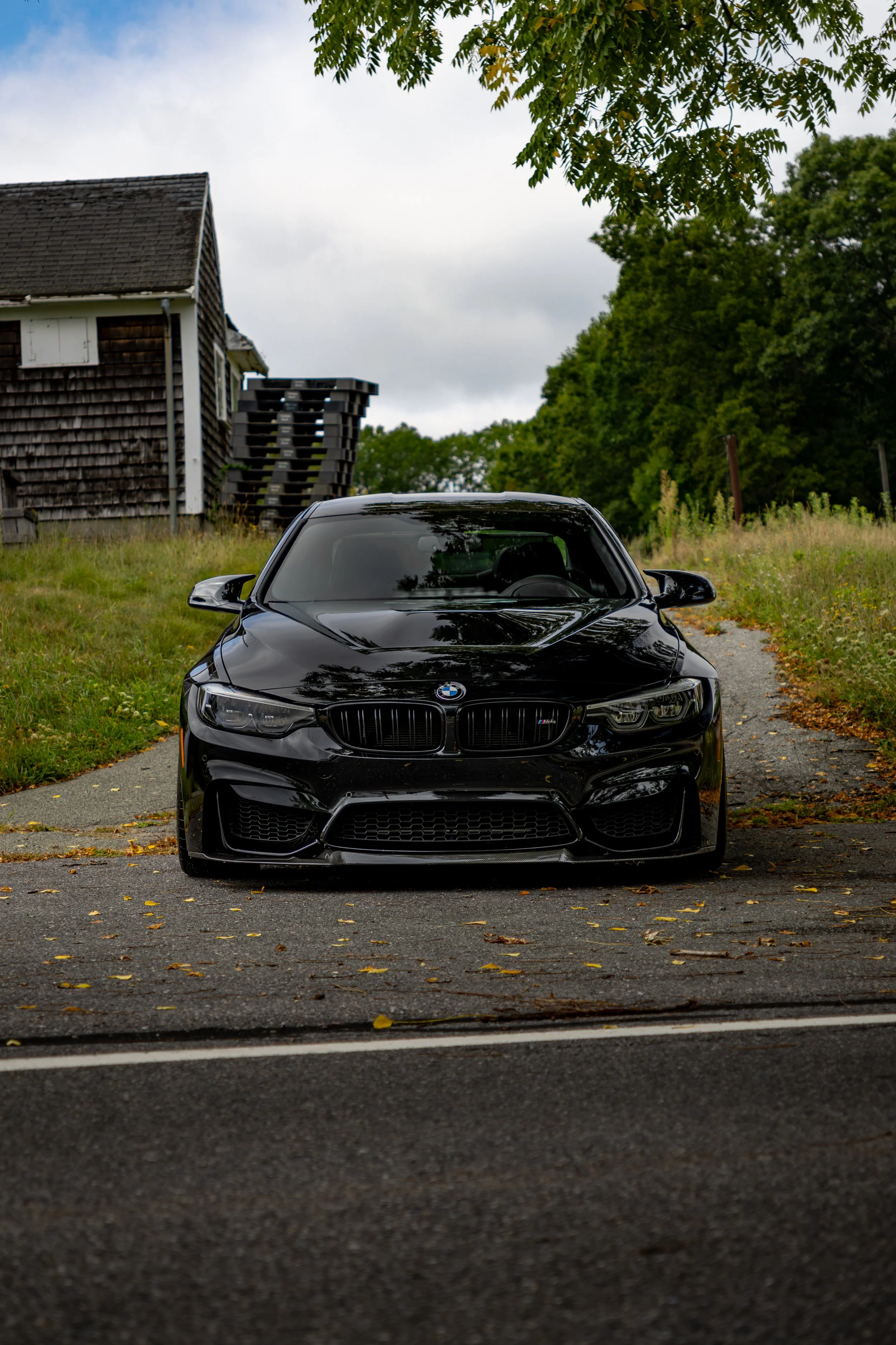 Head on, front angle shot of a Black 2019 BMW M4 CS parked on a driveway of a farm.