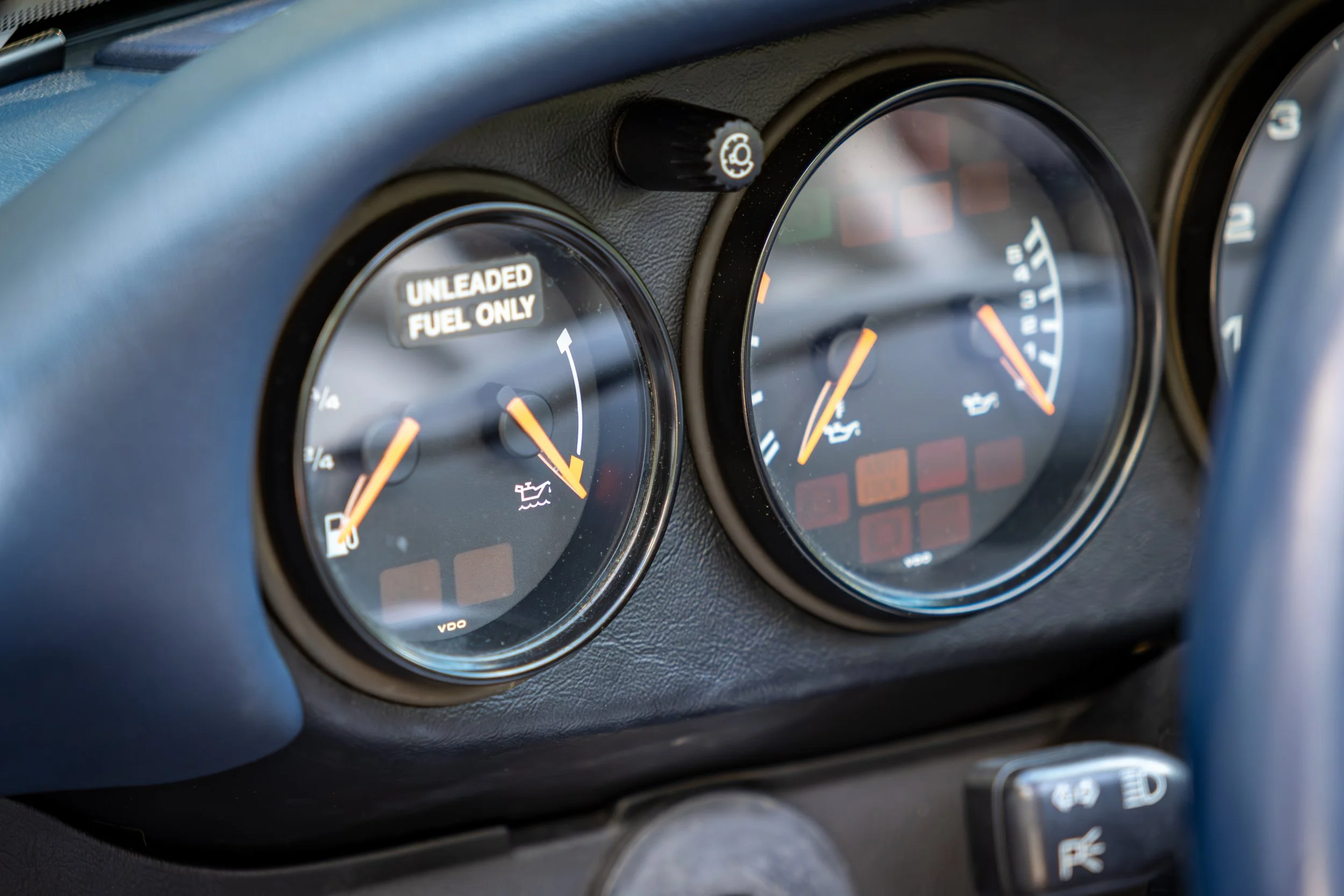Close-up of Porsche 993 911 dashboard showing three round gauges, including one with an oil can symbol, with a warning label that reads 'UNLEADED FUEL ONLY'.