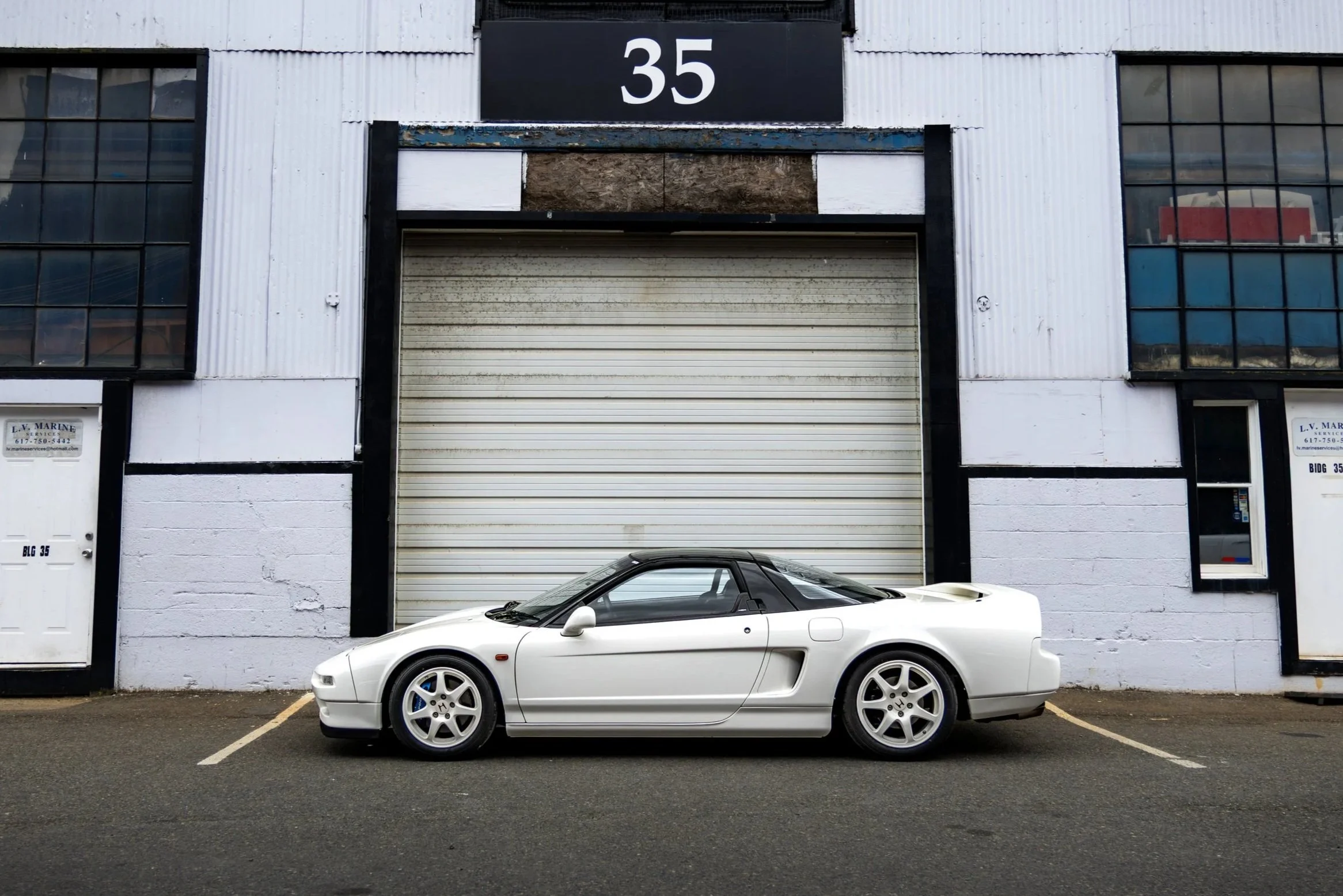 A white sports car parked in front of a building with a large garage door and the number 35 displayed above it.