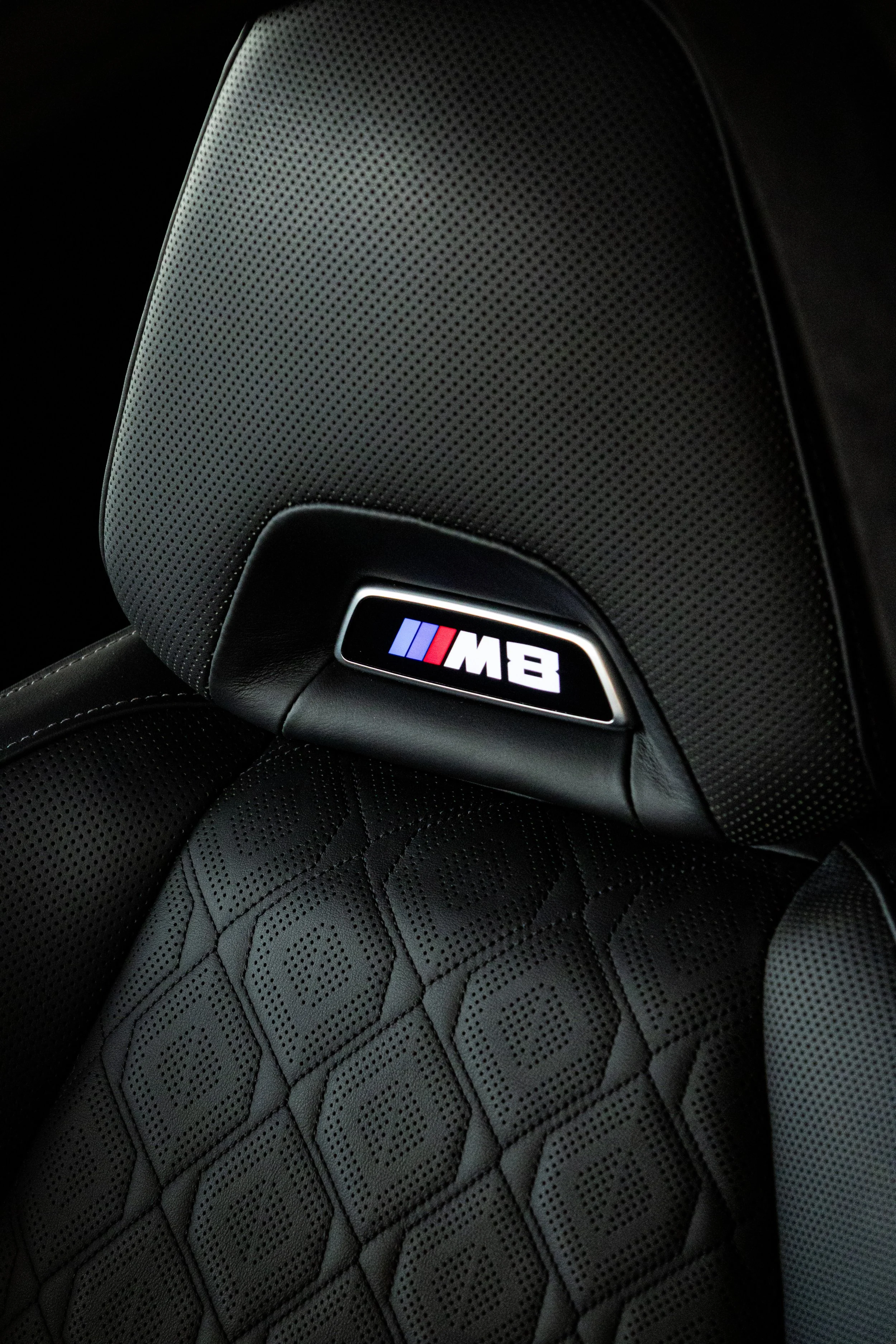 Close-up of a black leather car seat with the BMW M8 logo on the headrest.