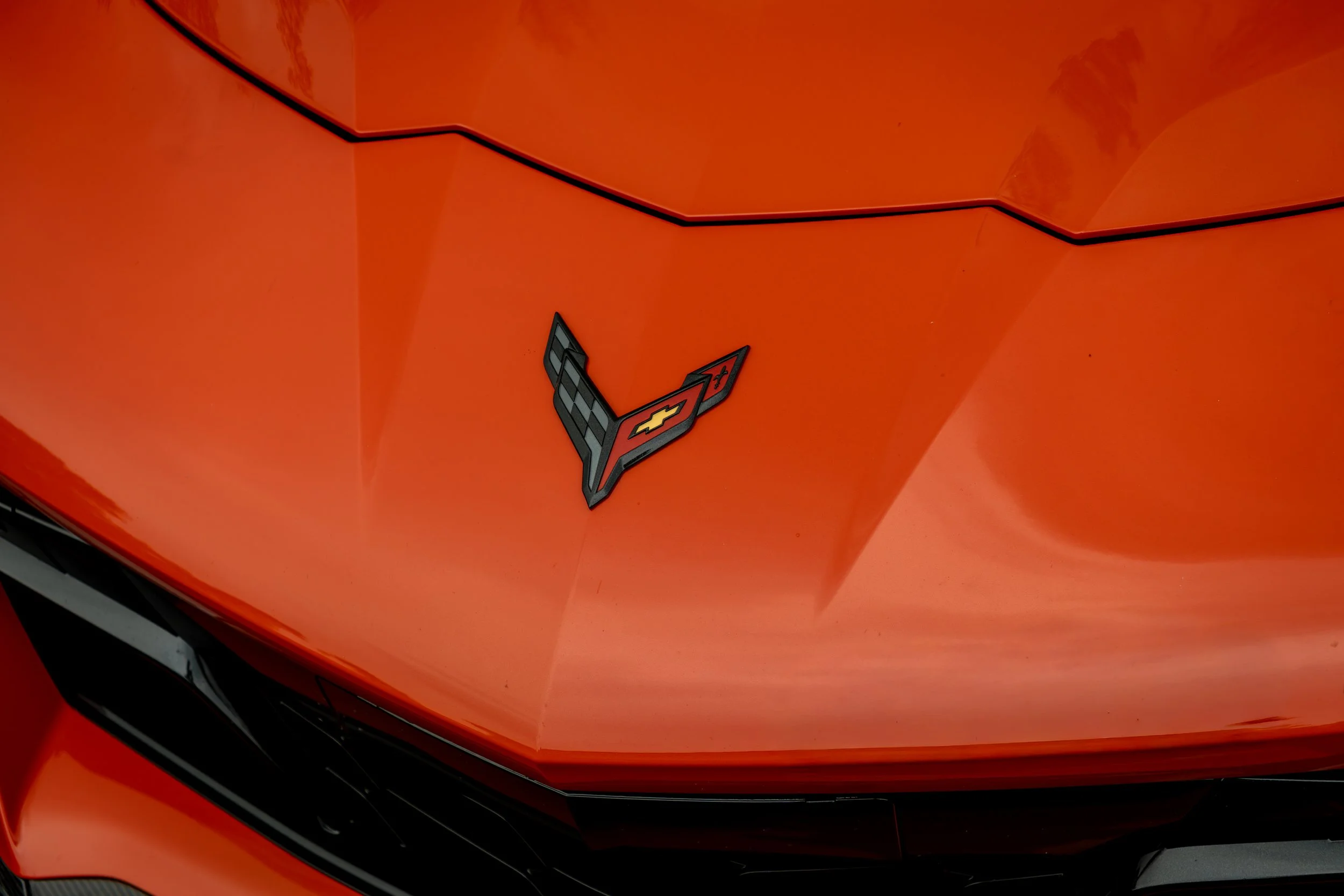 Close-up of the front of an orange 2026 Chevrolet Corvette ZR1 with a Chevrolet emblem and crossed flags badge.