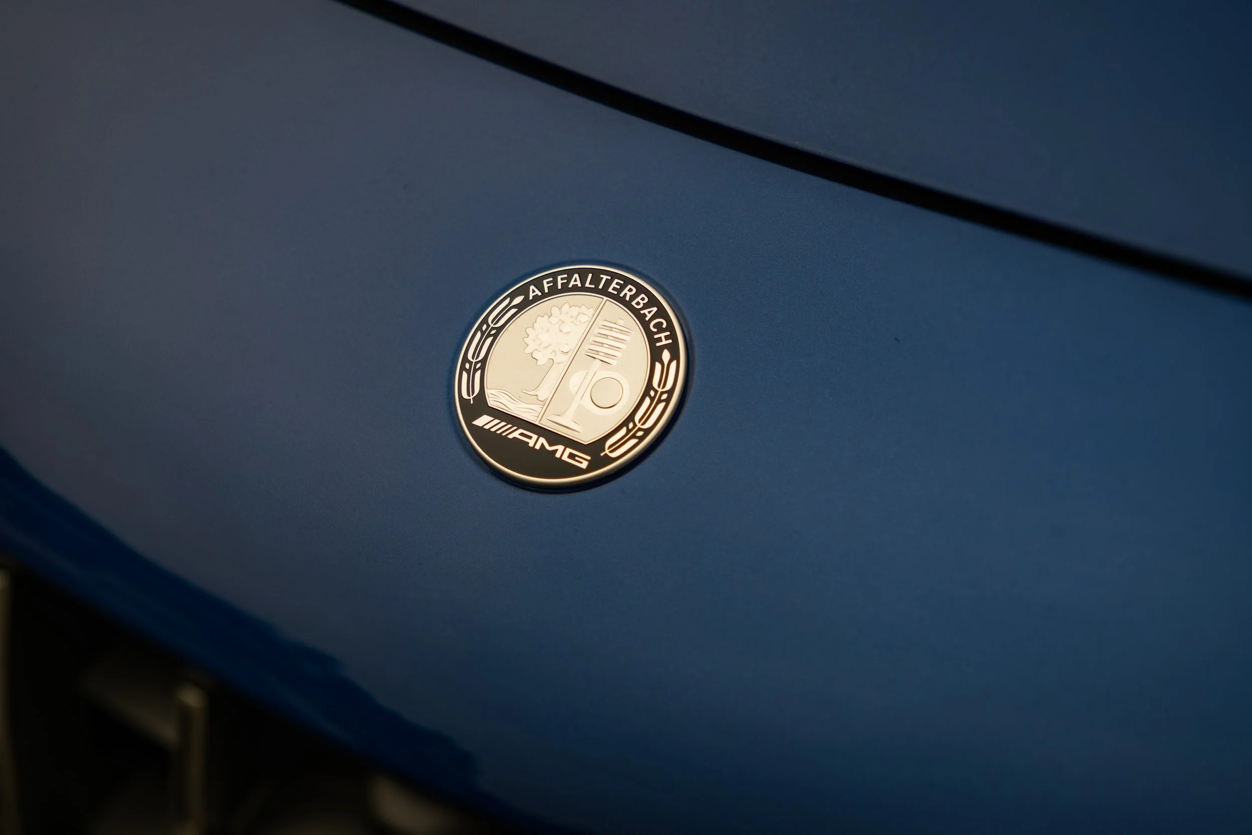 Close-up of a silver badge with the Mercedes-Benz logo and the words 'Affalterbach' and 'AMG' on a blue surface.