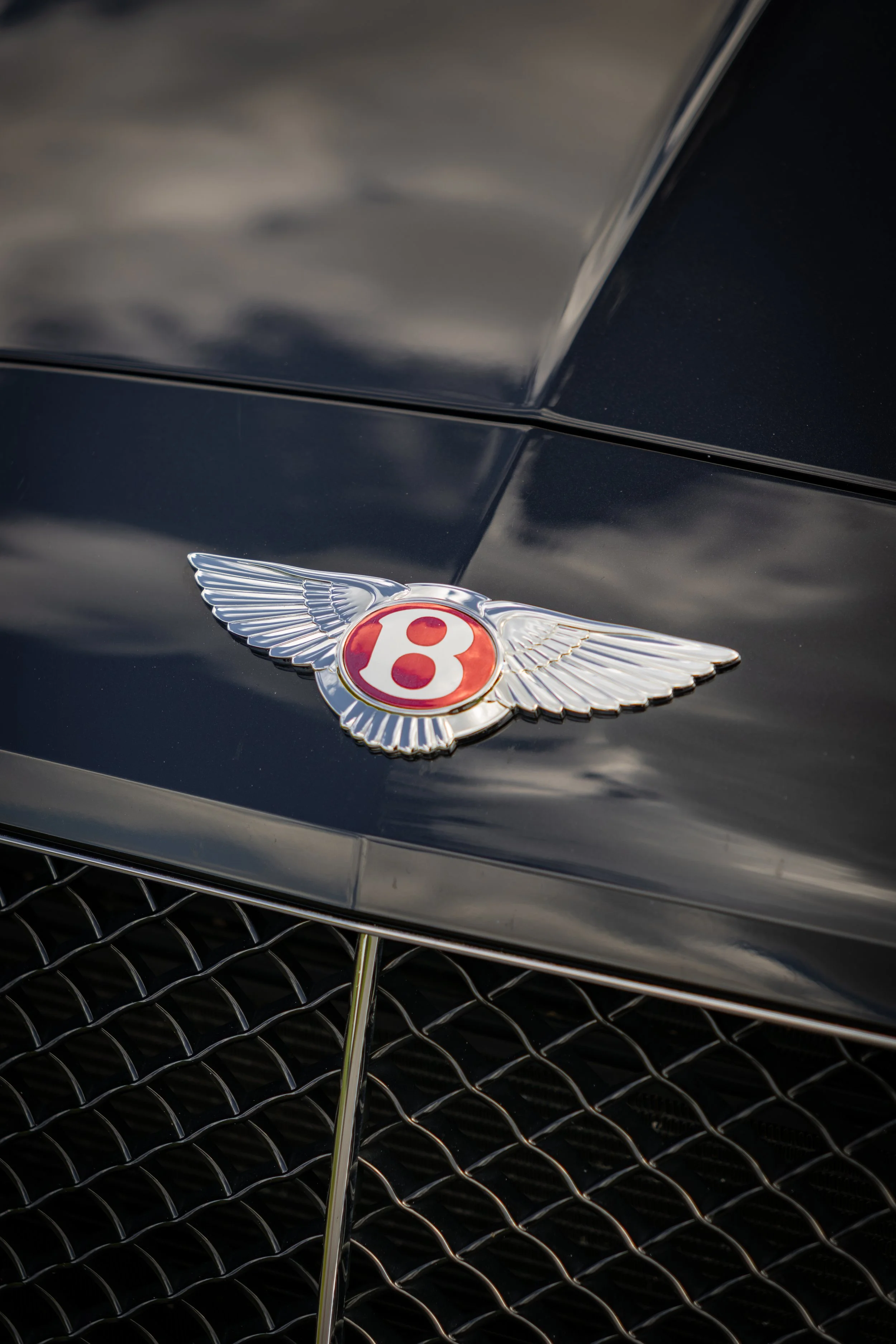 Close up of a Bentley emblem with a red center on  a black Bentley Continental GT V8 S