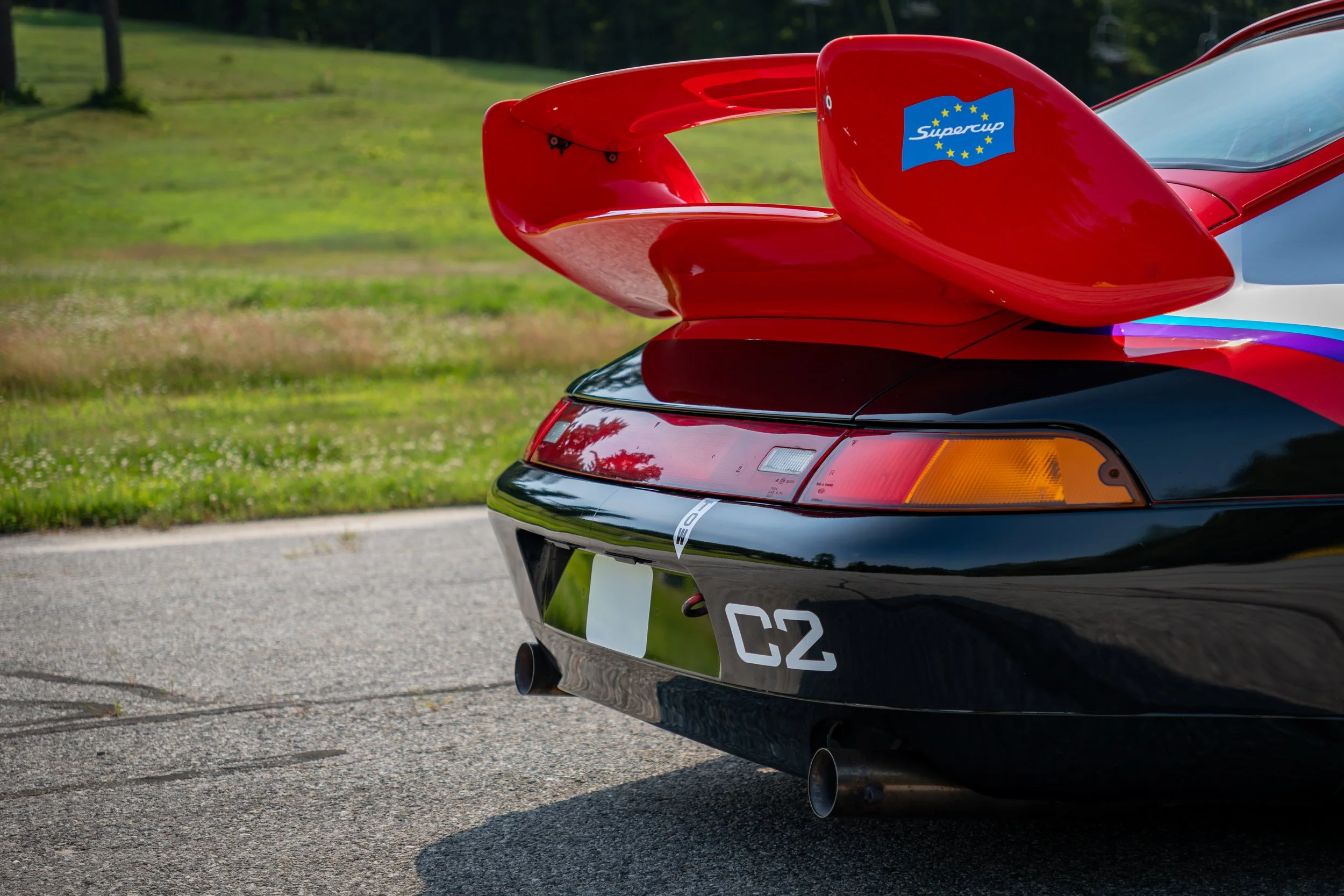 Close-up of the rear of a red Porsche GT2 Supercup race car with a prominent rear wing, a sticker that says 'Supercup' with a European Union flag design, and a black and white license plate. 