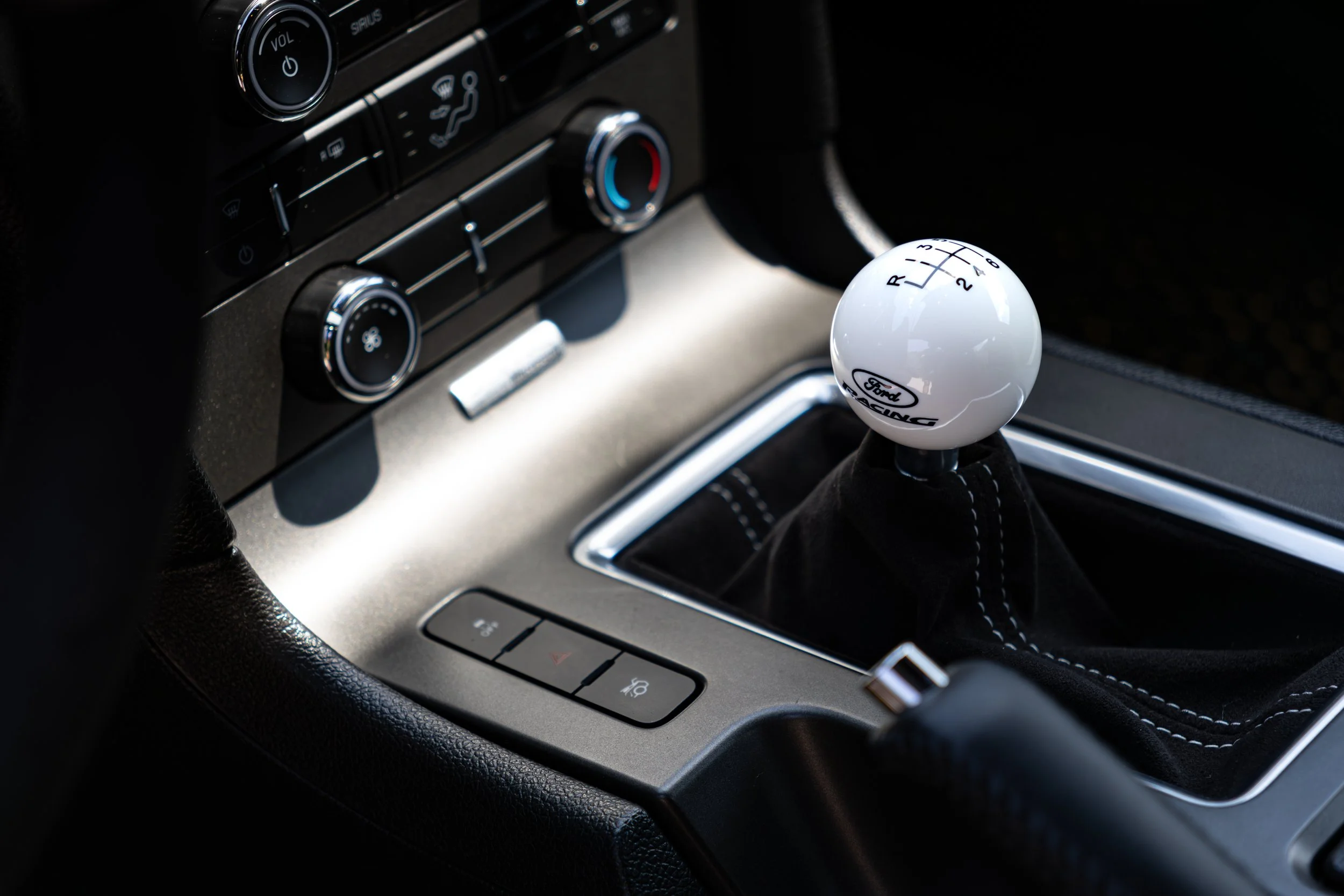 Close-up of Mustang Boss 302 center console showing a white Ford Racing gear shifter with a six-speed pattern, surrounded by climate control buttons and knobs.