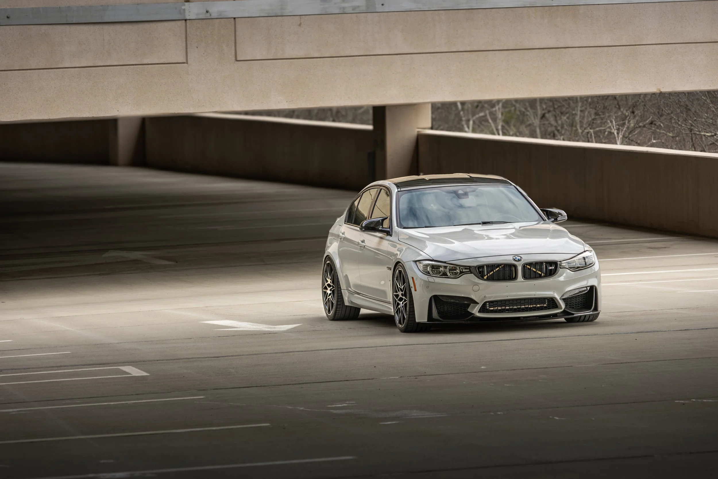 A white 2009 BMW M3 parked alone in an outdoor parking garage with concrete walls and an overhang.