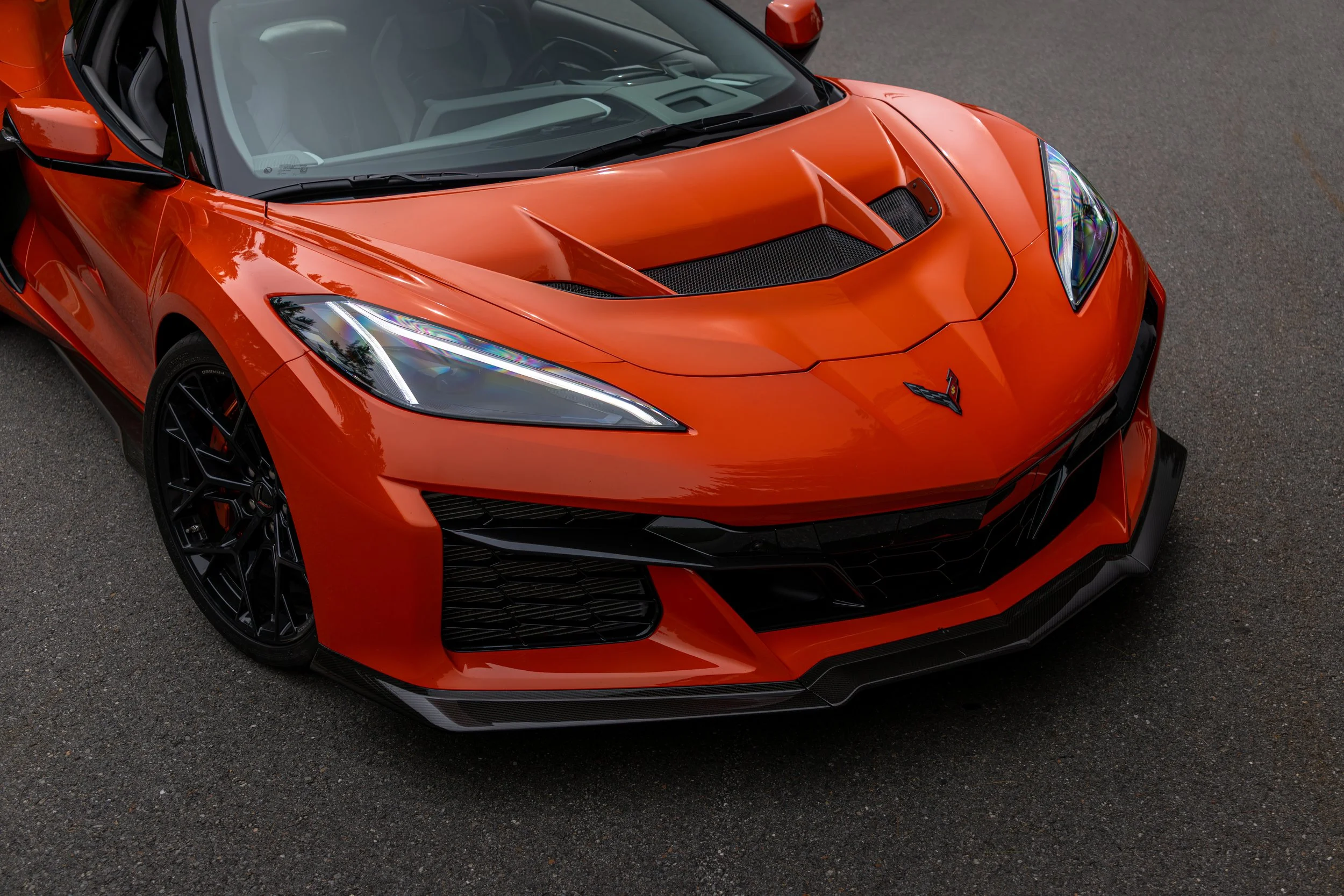 Orange 2026 Corvette ZR1 with an extremely sleek design, black wheels, and a front grille, parked on a paved surface.