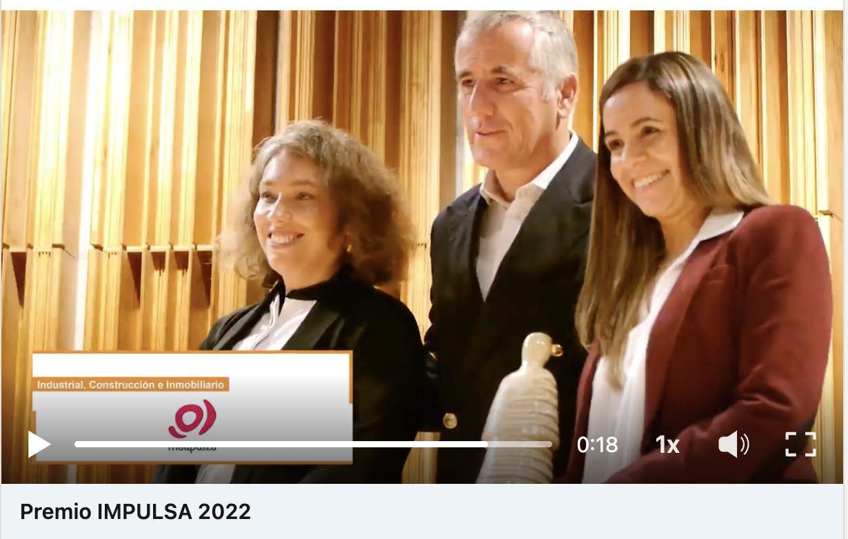 Tres personas en un evento de mujeres conectadas. Una mujer con cabello rizado, otra con cabello liso y castaño y un hombre con cabello gris, sonriendo frente a una pared de madera, con un banner que dice 'Industrial, Construcción e Inmobiliario'.