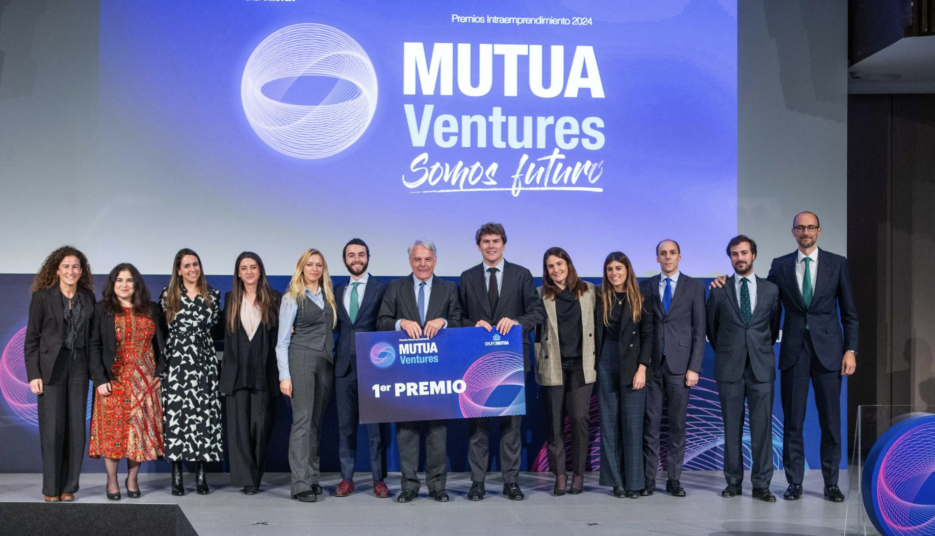 Grupo de personas en un escenario en una ceremonia de premios, con un fondo que dice 'Mutua Ventures Somos futuro' y una pantalla grande donde se lee Primer Premio 'Premios Intraemprendimiento 2024'.