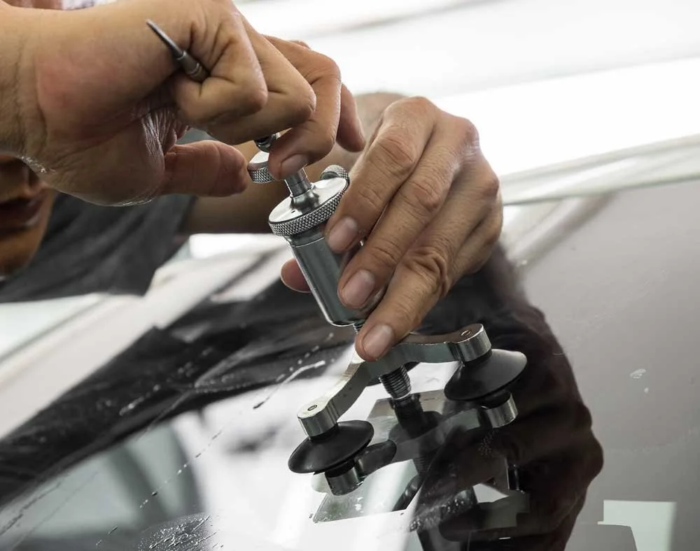 A person using a polishing tool on a car's surface, wearing gloves and focusing on a small area.