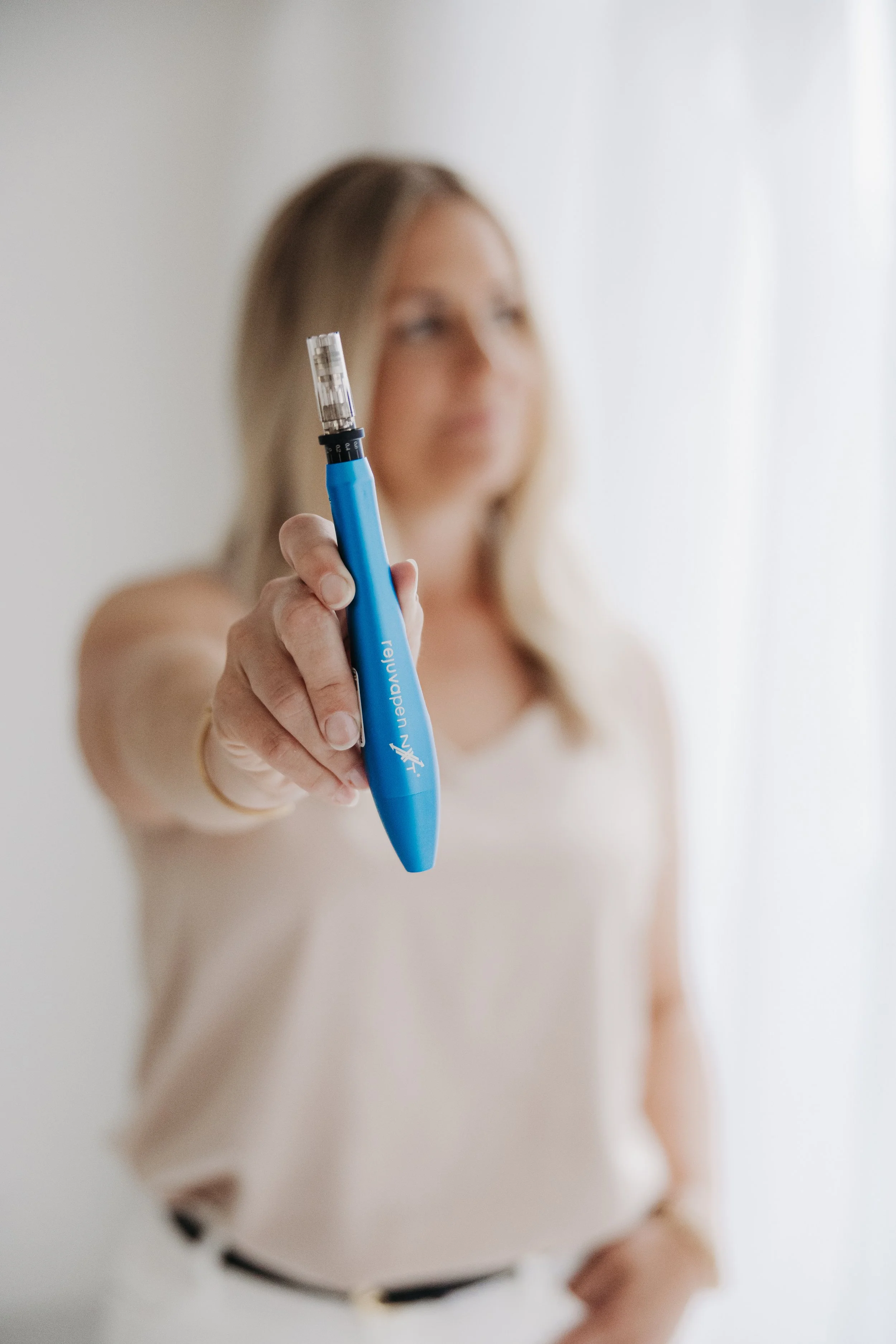 Close-up of a person holding Rejuvapen NXT professional microneedling device, with the person's face blurred in the background.
