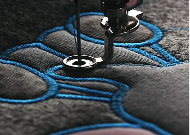 A sewing machine stitching black fabric with blue thread.