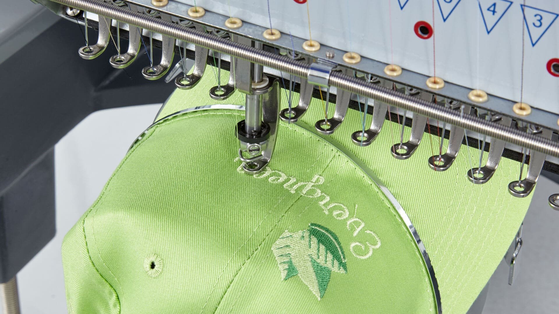 Embroidery machine stitching the logo onto a lime green fabric hat.