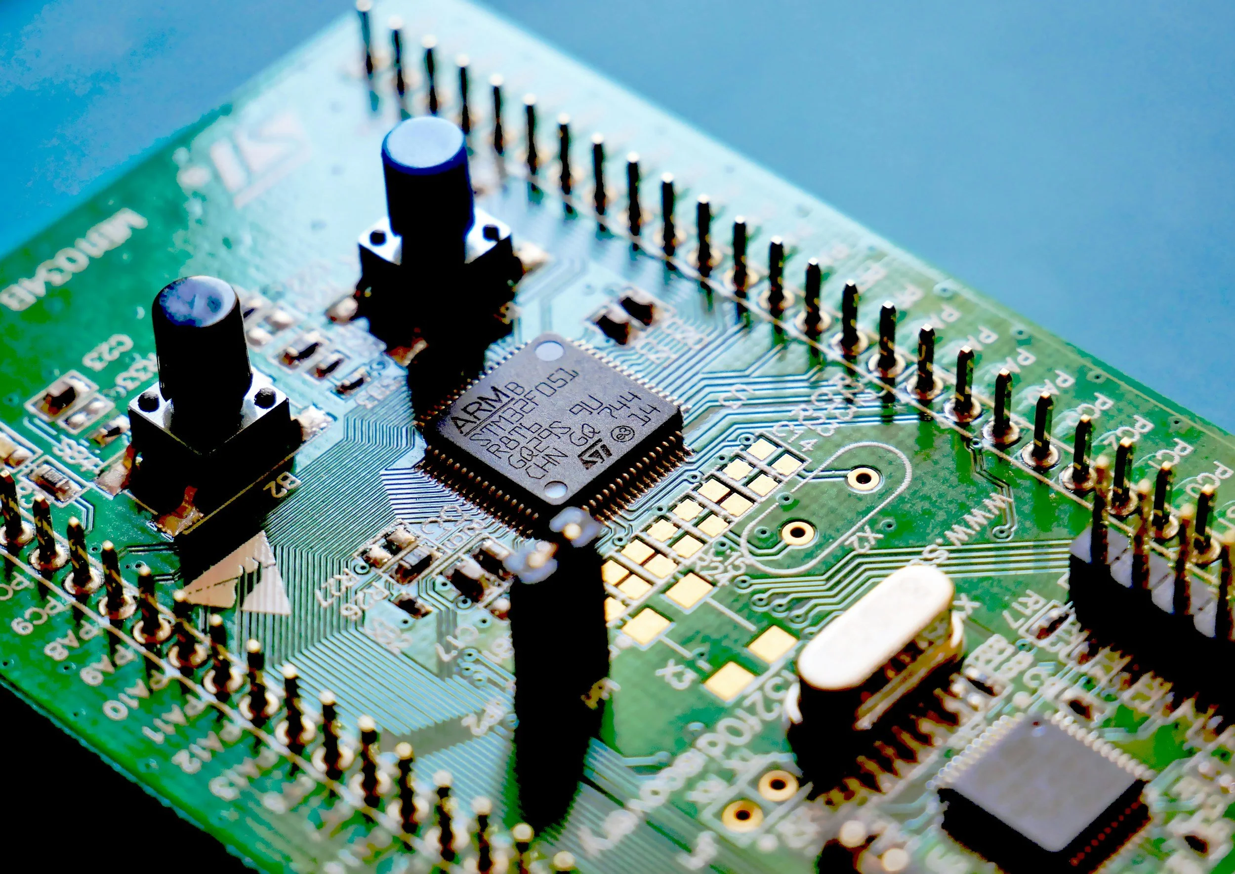 Close-up of a green printed circuit board (PCB) with black capacitors, an integrated circuit chip, and various electronic components.