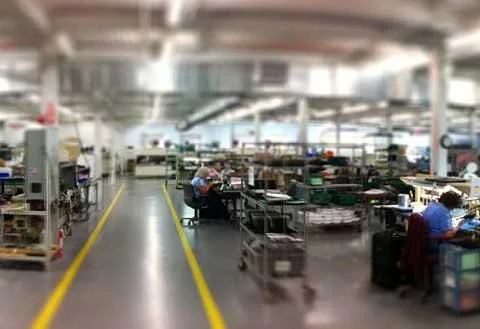 Factory or assembly line workspace with workers at their stations, surrounded by tools and equipment.
