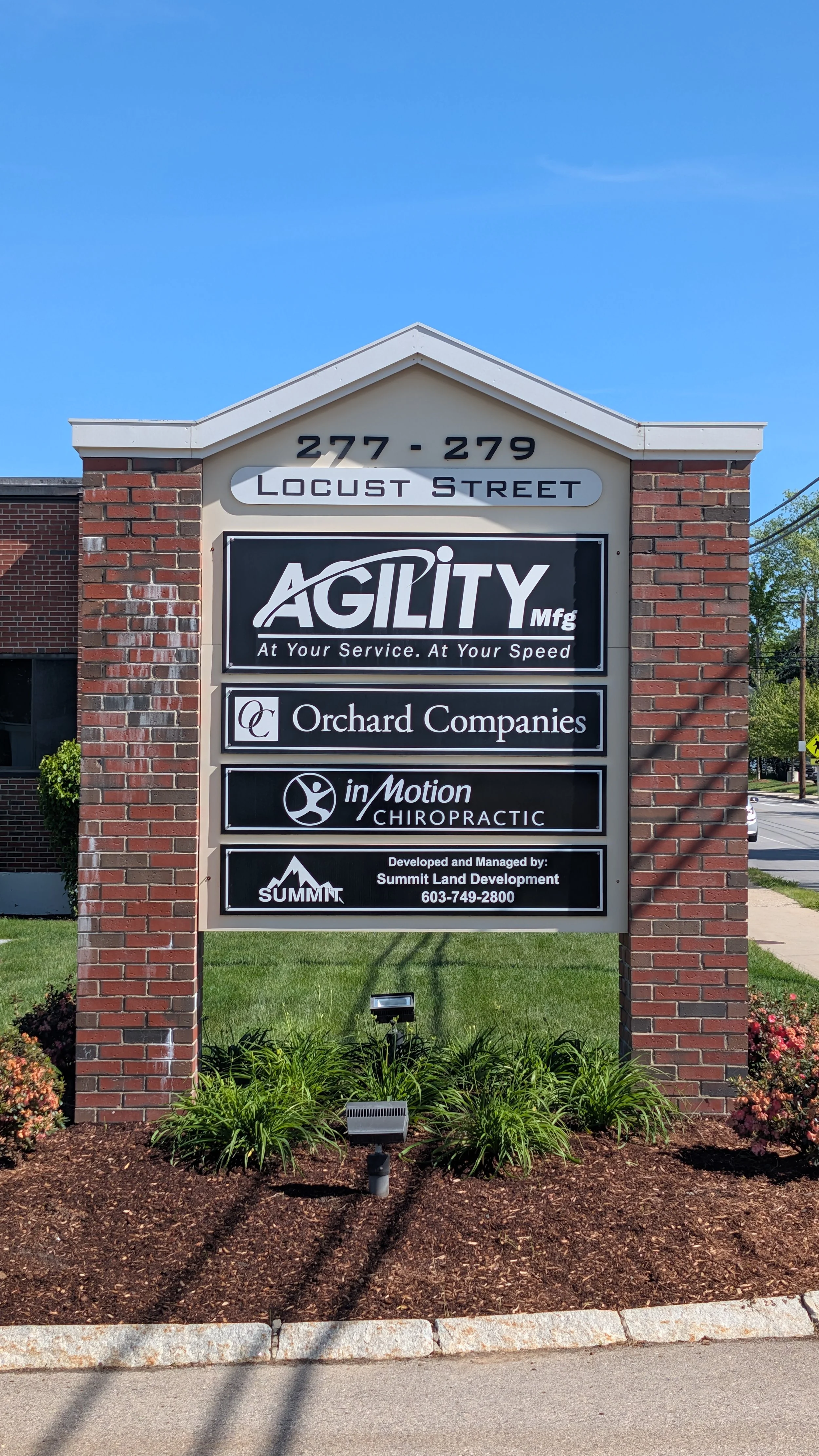 Sign listing businesses at 277-279 Locust Street, including Agility Manufacturing, Orchard Companies, in Motion Chiropractic, and Summit Land Development, with a clear blue sky in the background.
