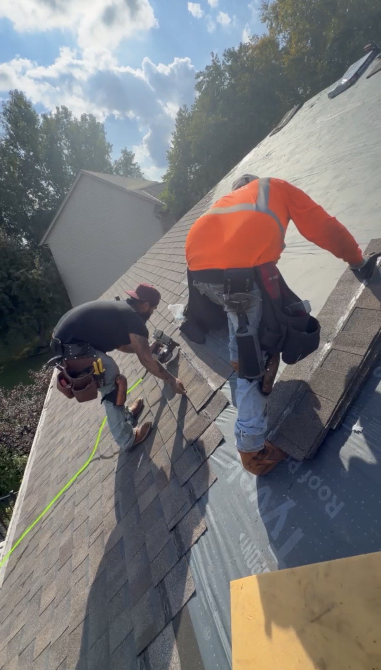 Two workers installing or repairing shingles on a sloped roof during daytime with a partly cloudy sky in the background. In Maple Grove MN