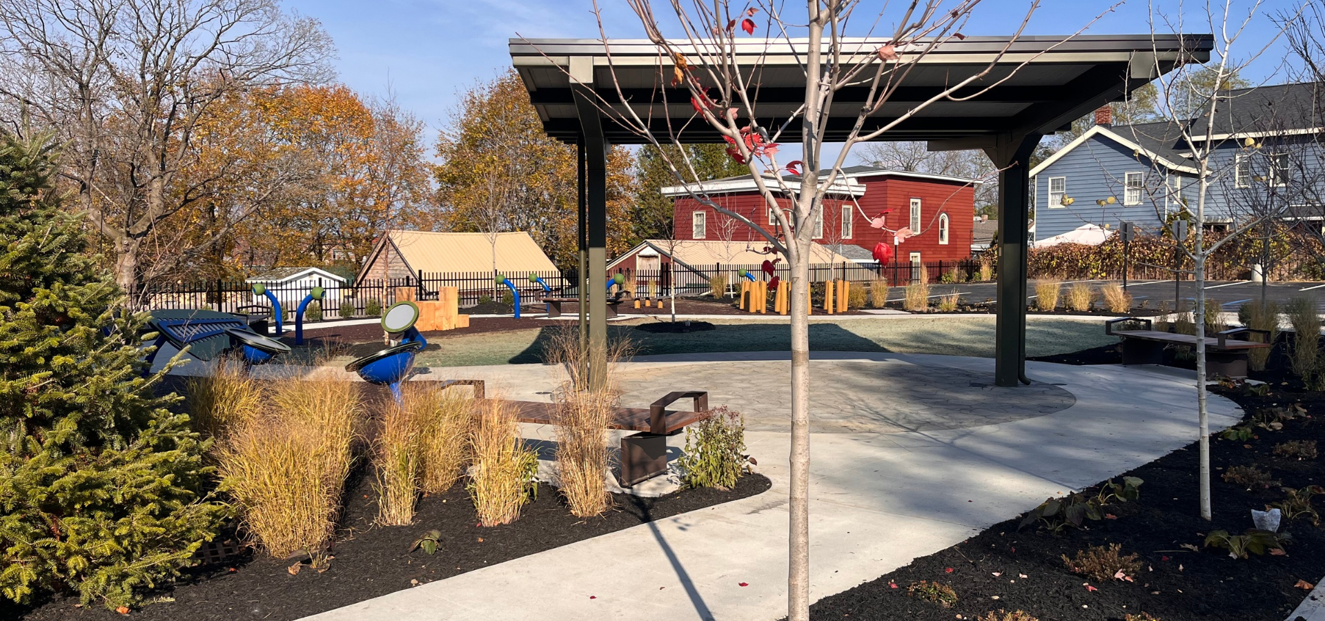 Outdoor fitness playground with exercise equipment, landscaped paths, pavilion, and colorful historic homes in autumn