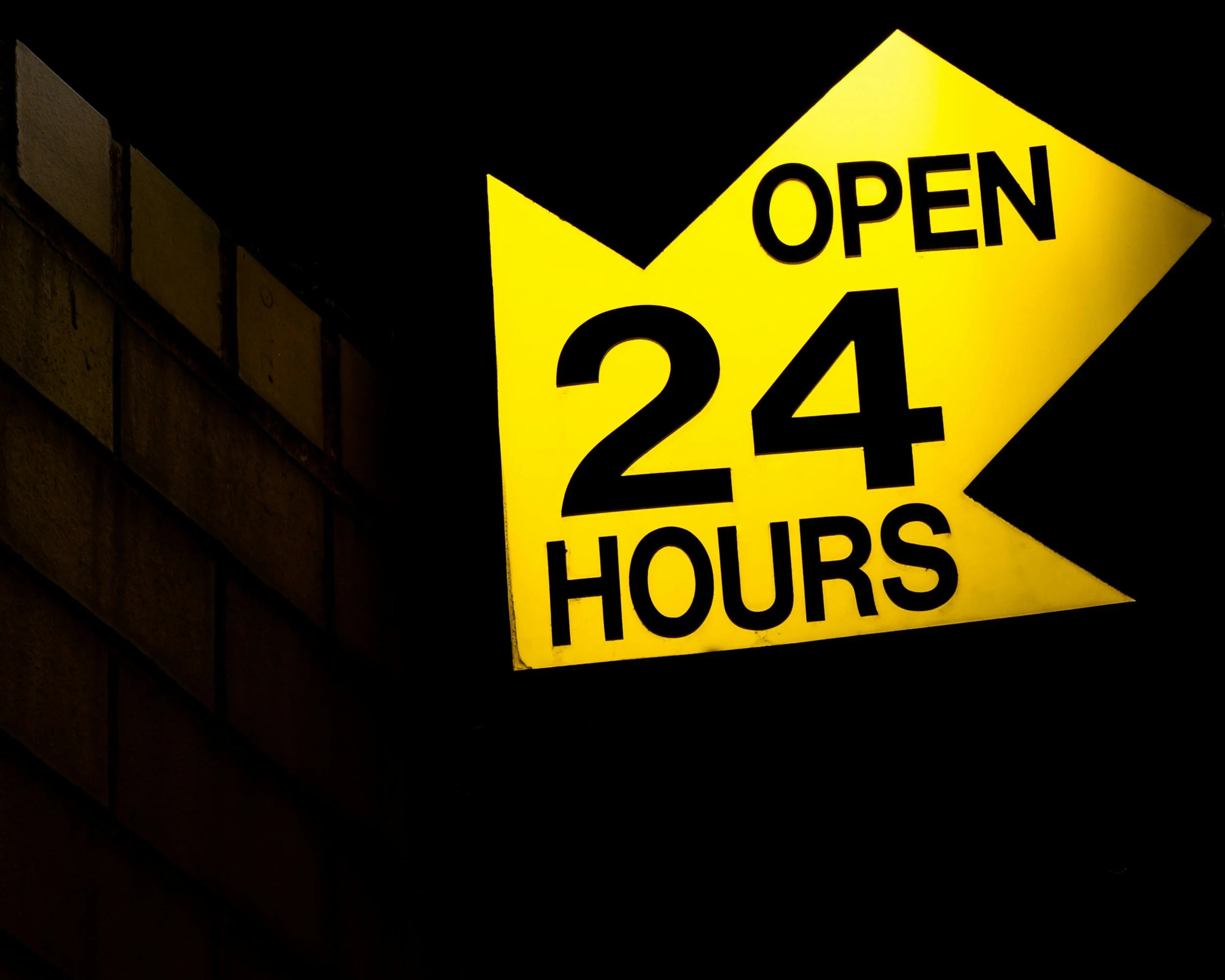 Bright yellow illuminated sign reads 'Open 24 Hours' against a dark night background.