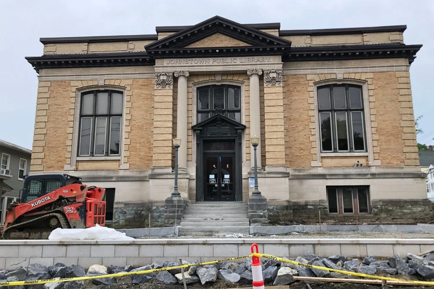 Construction work outside the Johnstown Public Library showing a small excavator and caution tape.