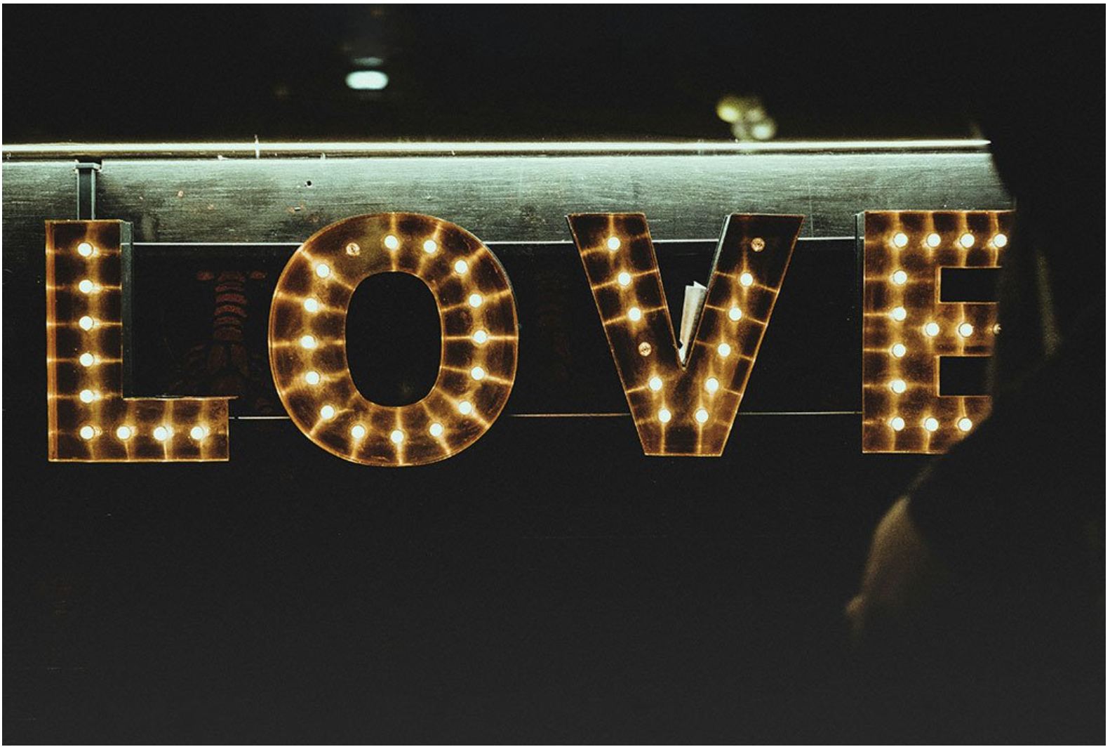  illuminated decorative sign spelling out the word "LOVE" with light bulbs, mounted on a dark wall.