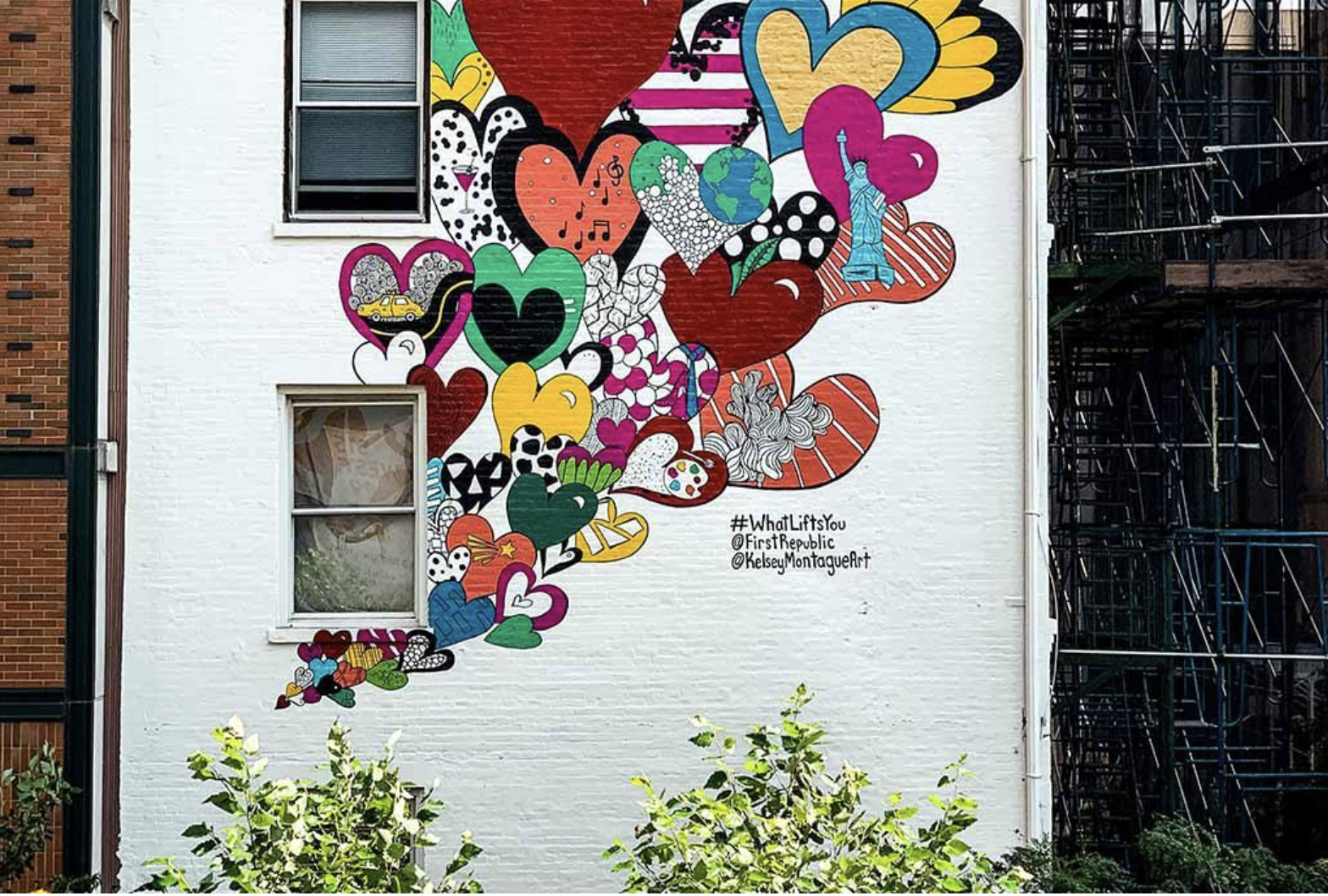 Colorful mural with hearts, Earth, Statue of Liberty, and various designs on a white building wall.
