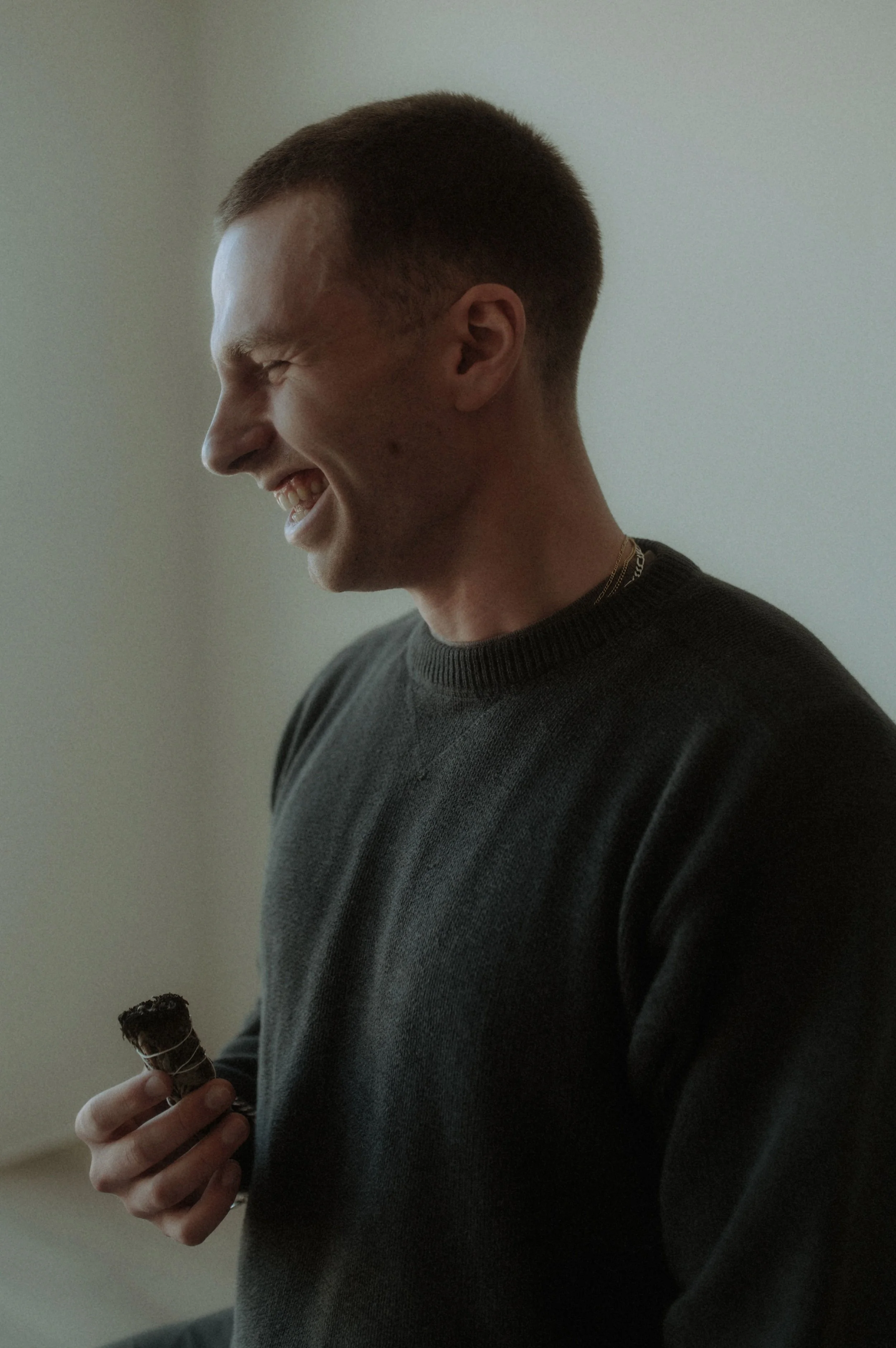 A young man with a short haircut smiling and holding a bundle of sage.