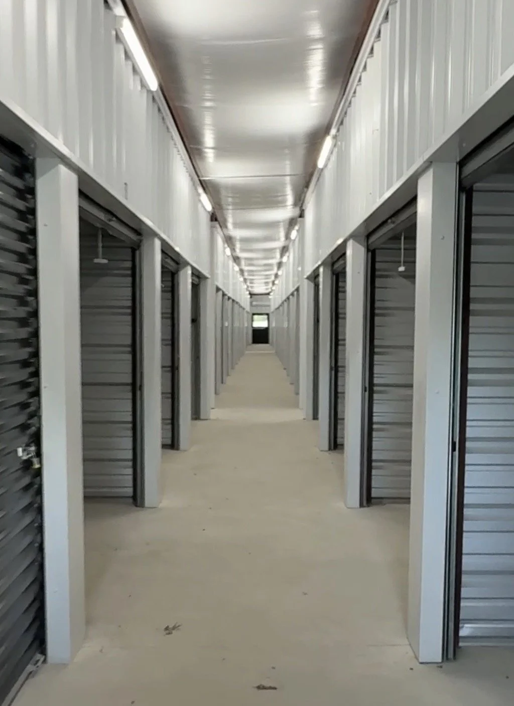 Long corridor of storage units with metal roll-up doors in a storage facility.
