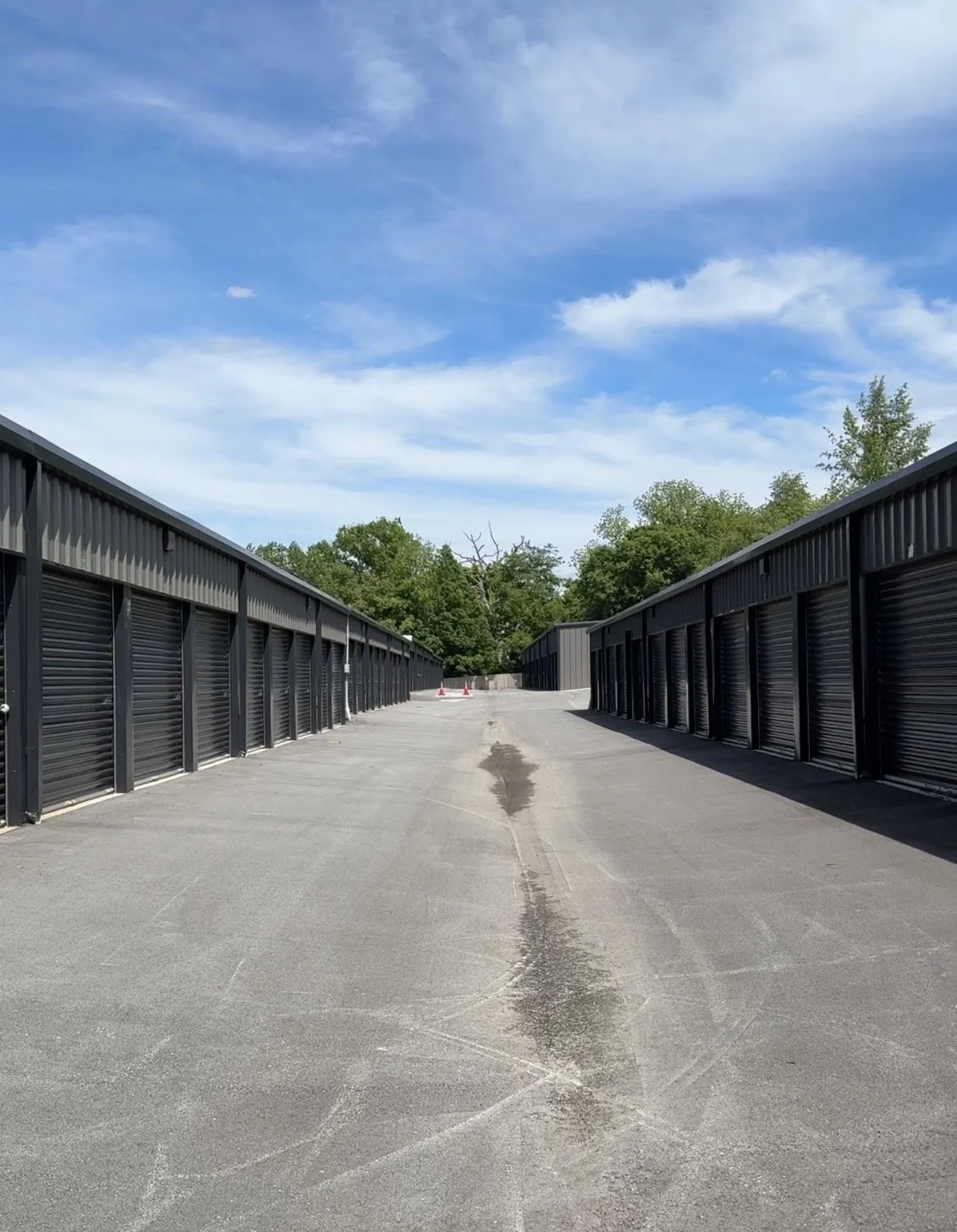a view of Goshen mini storage with storage units on both sides, under a partly cloudy sky, with trees in the background.