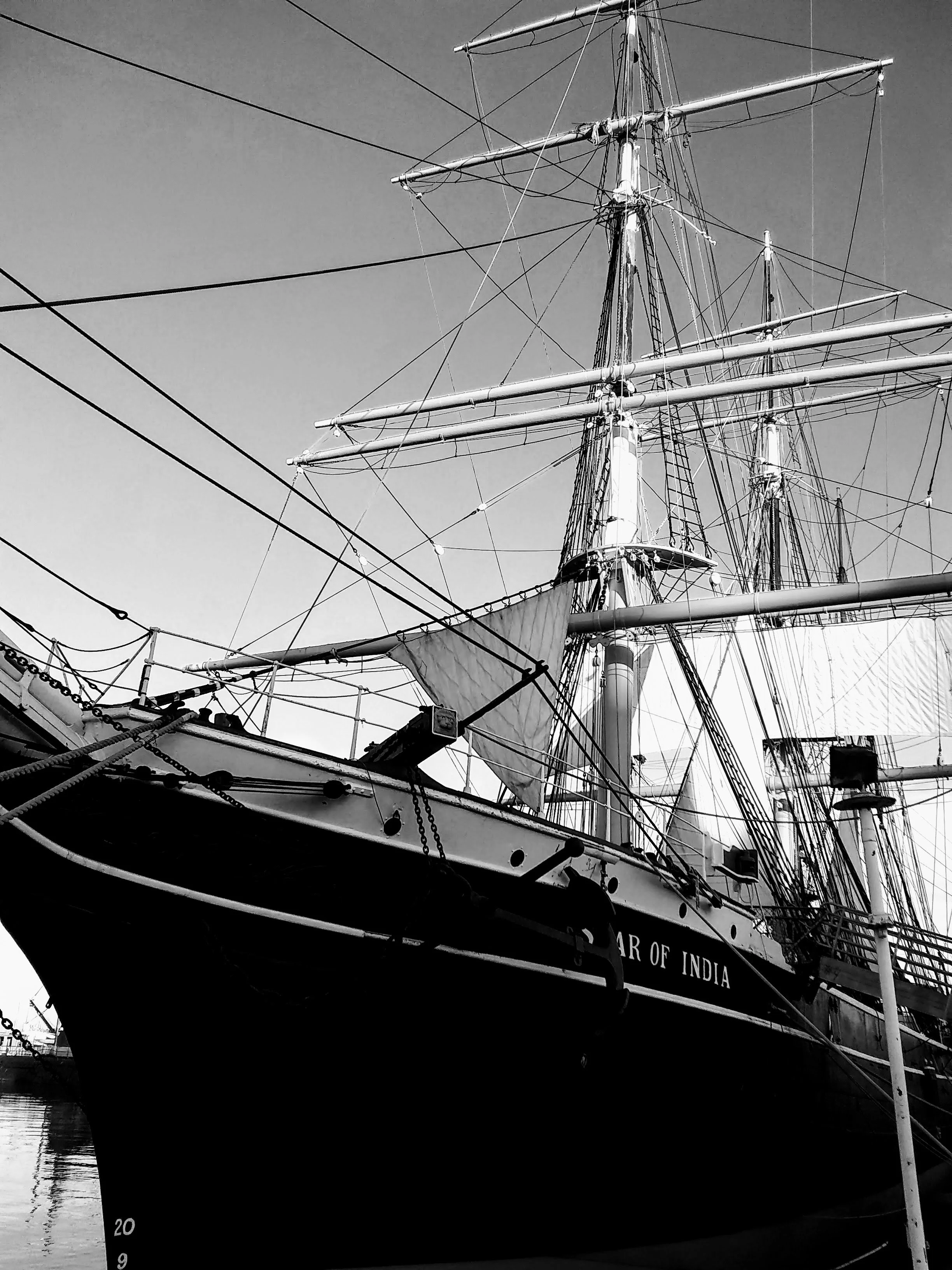 Black and white photo of a tall sailing ship docked at a harbor, showing its masts, rigging, and hull with the words 'Star of India' visible on the side.