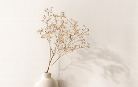 A white vase with dried flowers on a plain white wall.