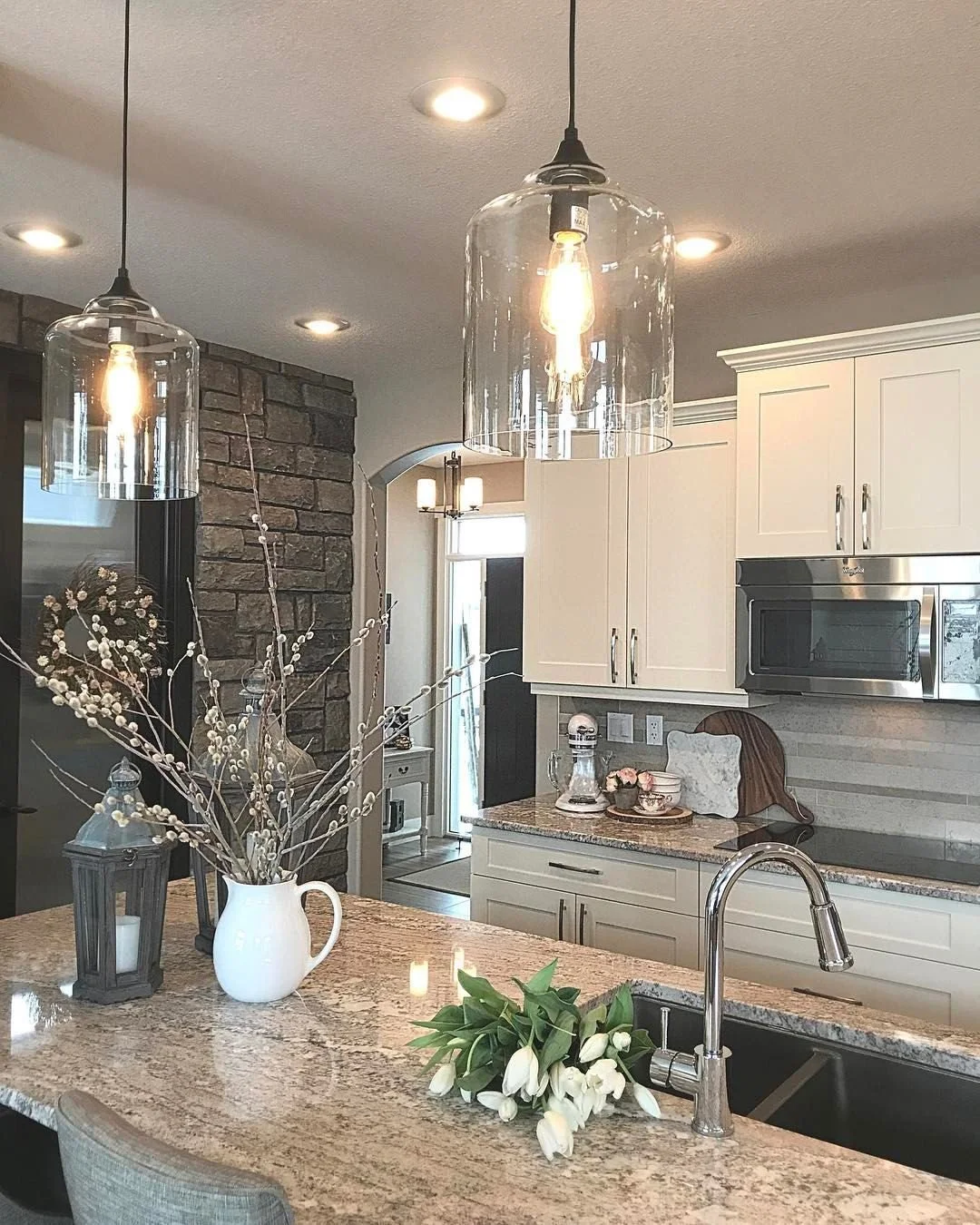 Modern kitchen with pendant lights, white cabinets, granite countertop, flower arrangements, and stainless steel appliances.