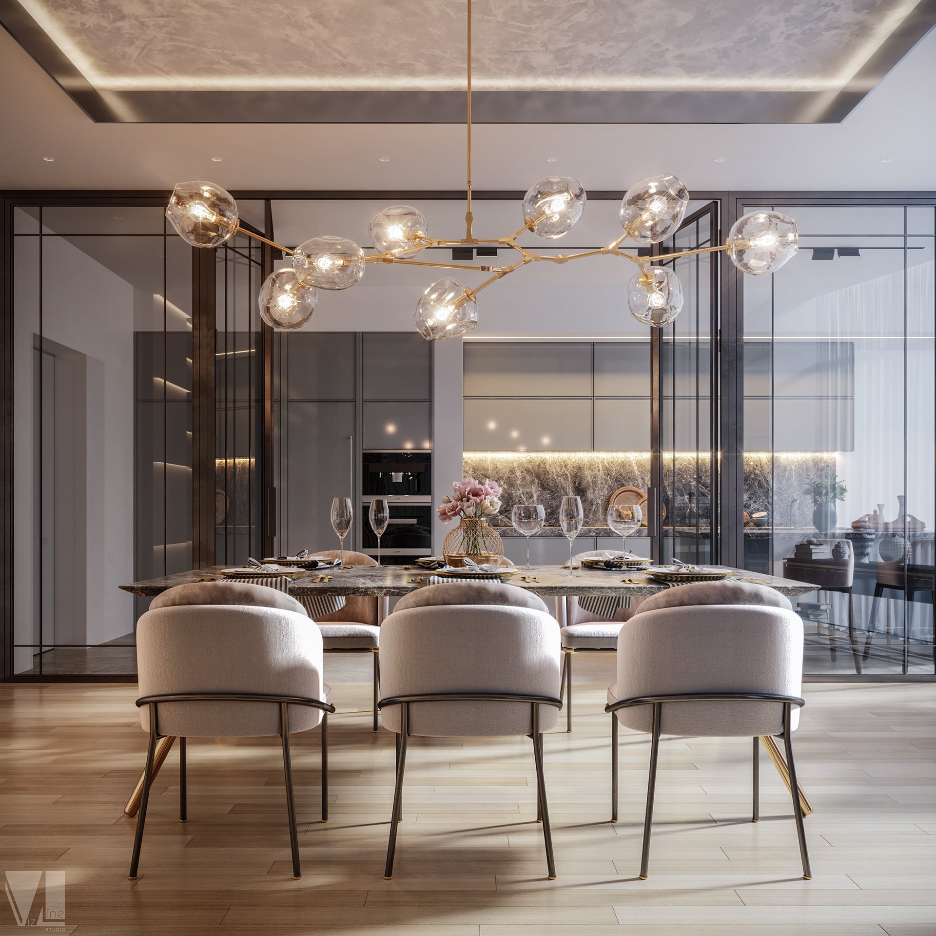 Modern dining room featuring eight white upholstered chairs around a dark, polished marble dining table set with glassware, plates, and cutlery. A gold chandelier with multiple glass globes hangs above. In the background, a kitchen area with white cabinets, a decorative vase with pink flowers, and a marble backsplash.