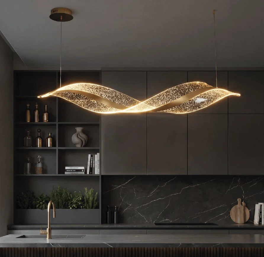 Modern kitchen with a unique wavy LED light fixture, dark cabinetry, black marble backsplash, gold faucet, and decorative items including vases and greenery.